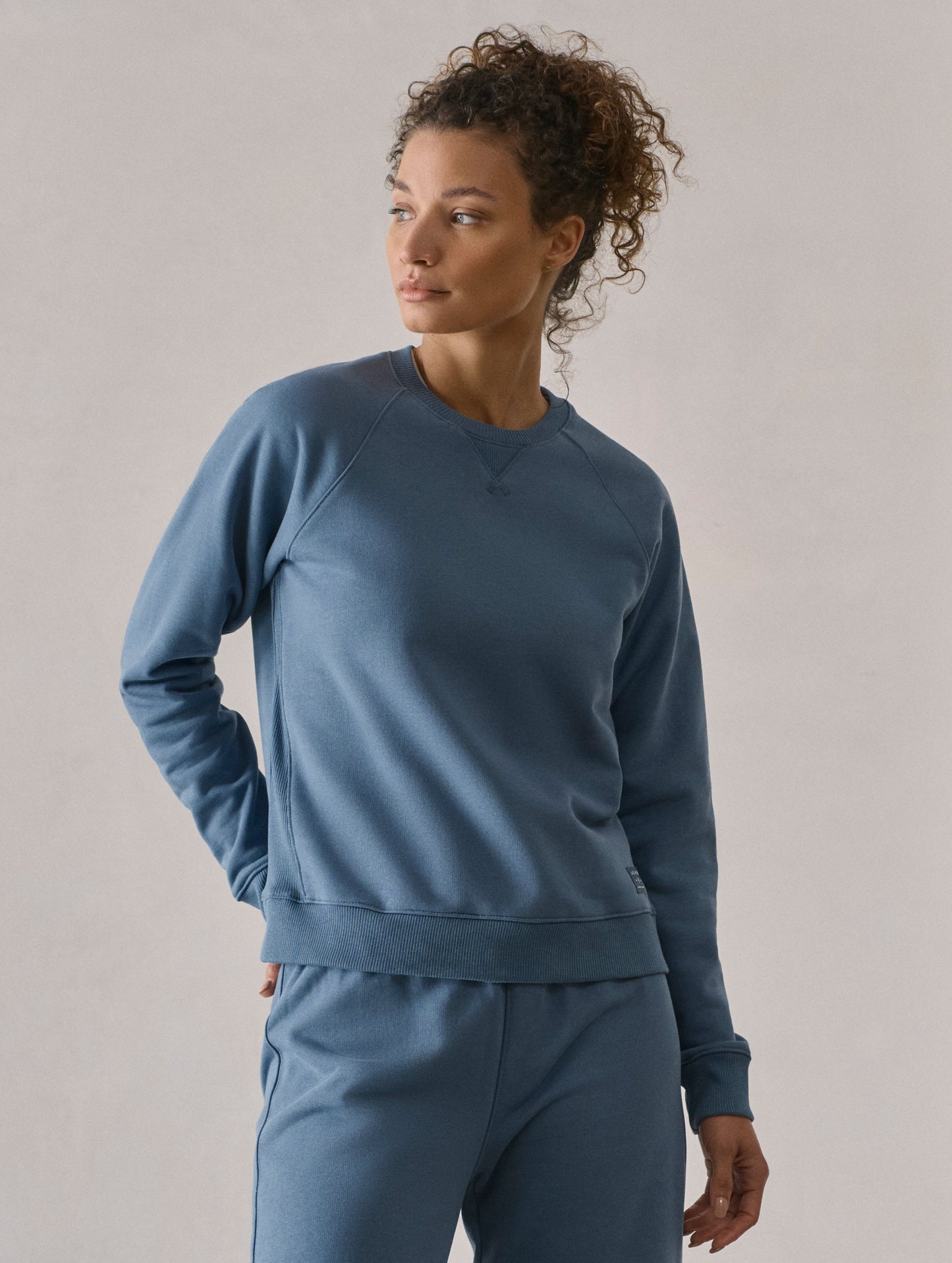 Front 3/4 upper-body view of woman wearing W Osa Raglan Sweatshirt in Coastal Blue from AETHER Apparel.