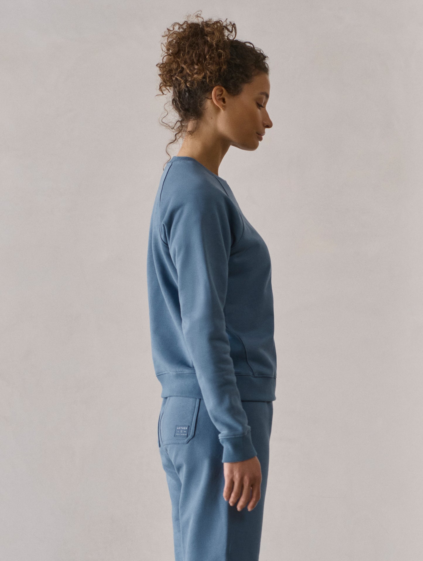 Right side profile upper-body view of woman wearing W Osa Raglan Sweatshirt in Coastal Blue from AETHER Apparel.