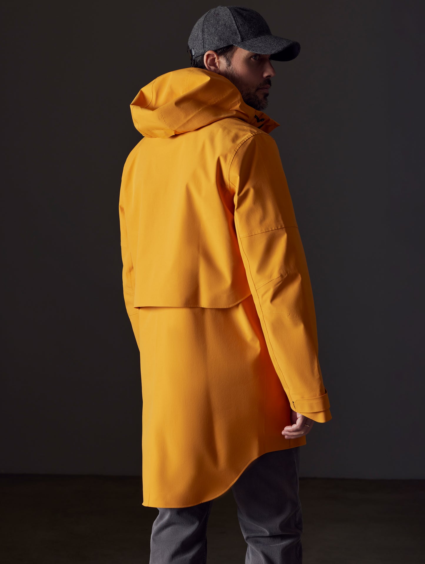 Rear 3/4 body view of man wearing Anders Rain Jacket in Midas Orange from AETHER Apparel.