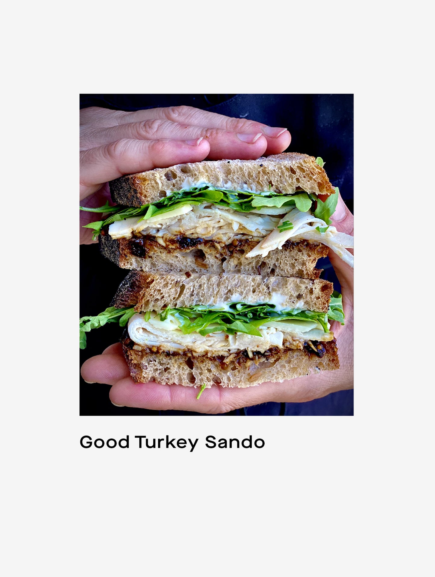Closeup image of hands holding Good Turkey Sando sandwich cut in half.
