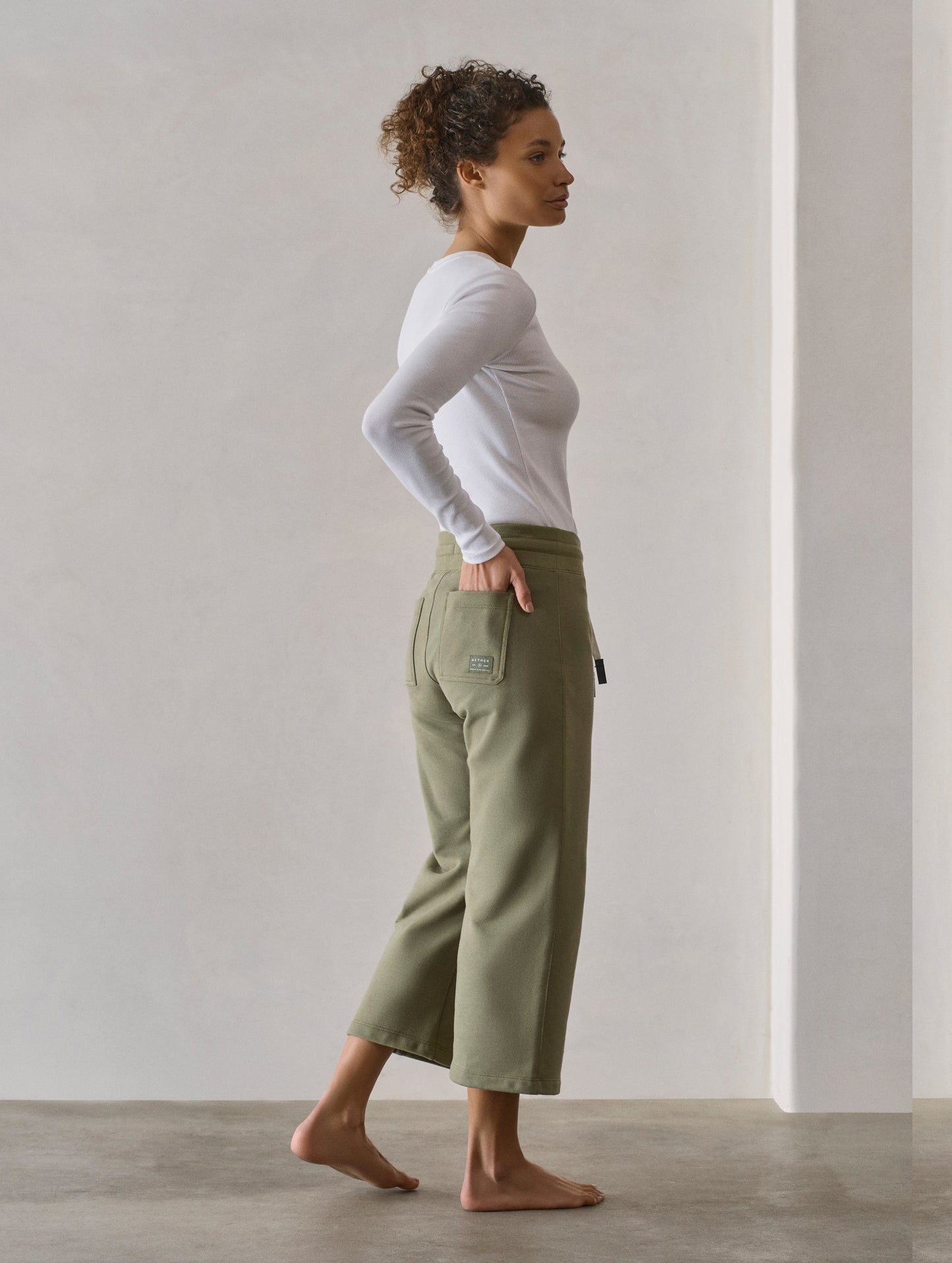 Right side profile full-body view of woman wearing W Osa Cropped Sweatpant in Fern Green from AETHER Apparel.