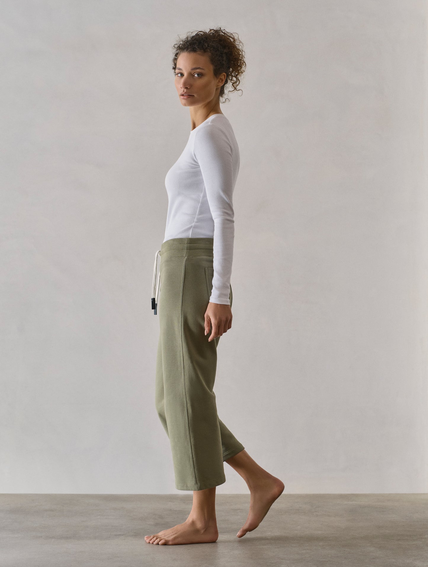 Left side profile full-body view of woman wearing W Osa Cropped Sweatpant in Fern Green from AETHER Apparel.