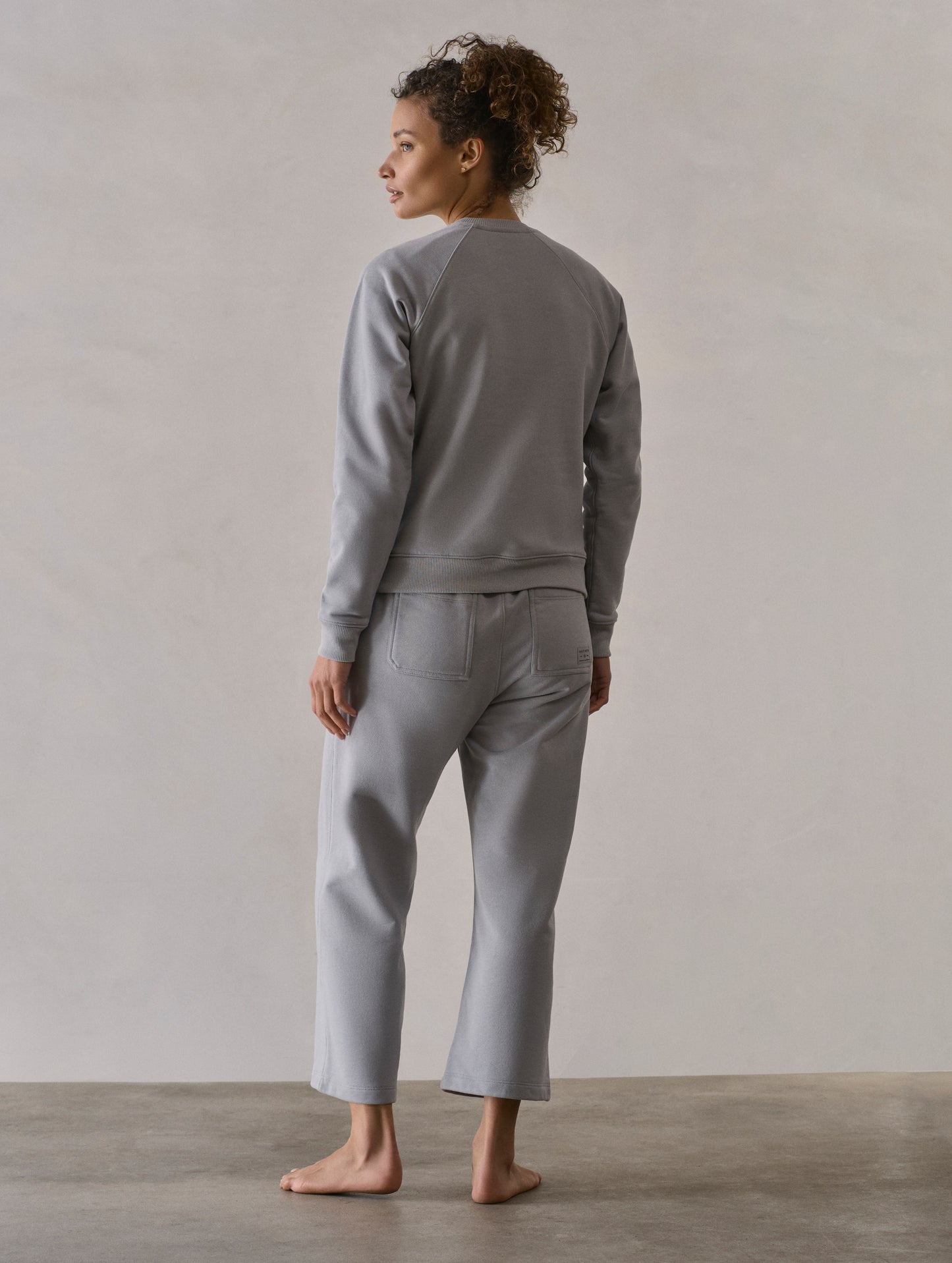Rear 3/4 full-body view of woman wearing W Osa Raglan Sweatshirt in Sky Grey from AETHER Apparel.