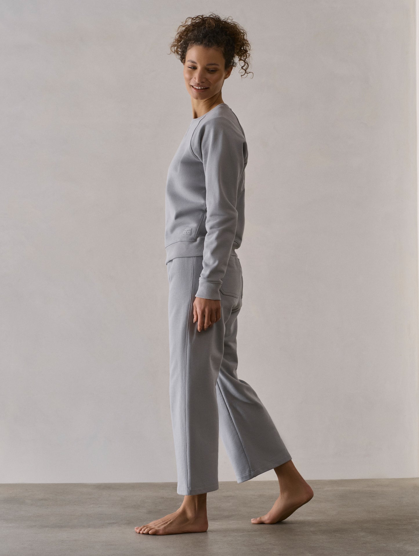 Left side profile full-body view of woman wearing W Osa Raglan Sweatshirt in Sky Grey from AETHER Apparel.