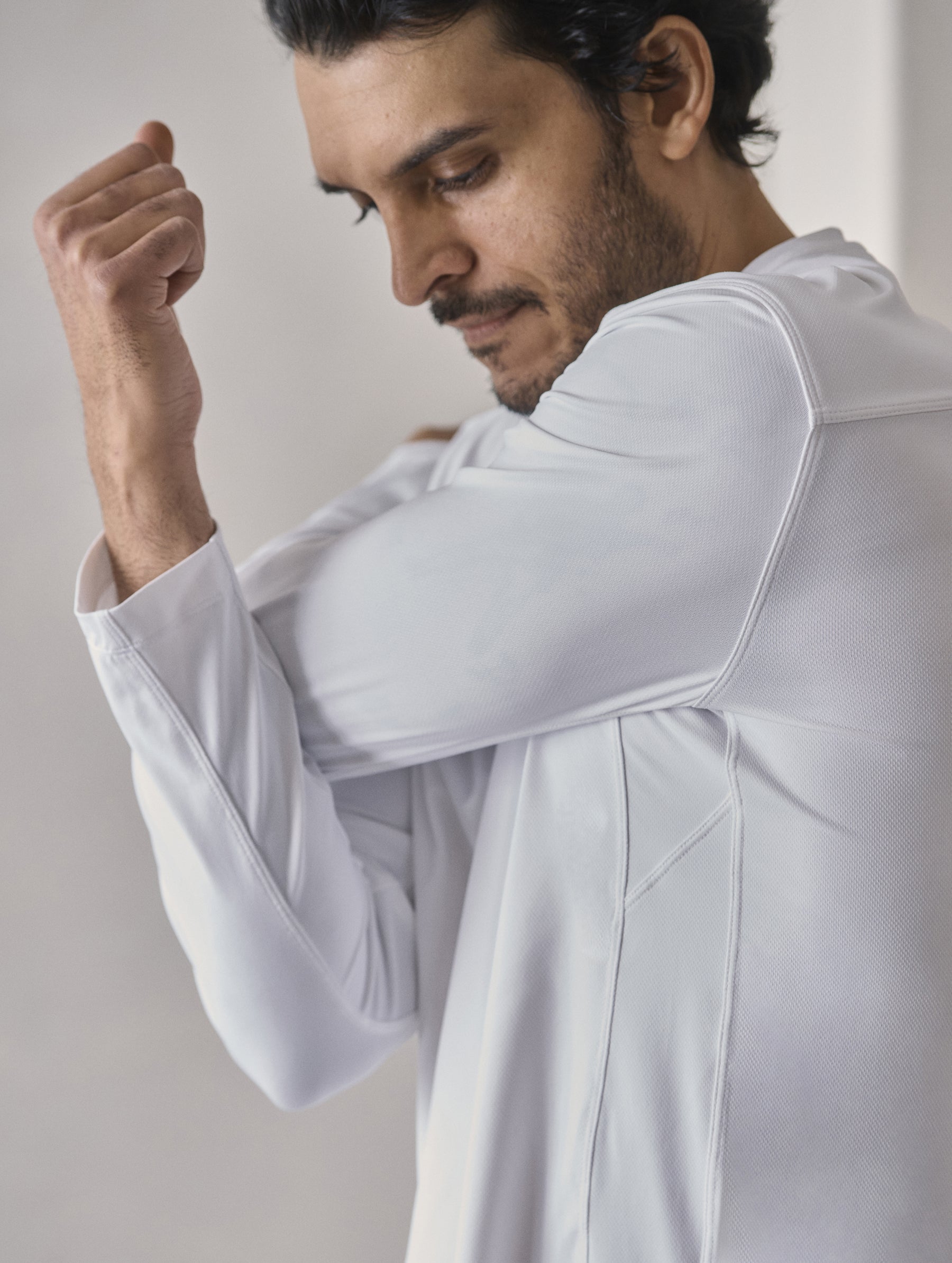 Upper body view of man stretching arms wearing the Adventure Performance Long-Sleeve Tee in White from AETHER Apparel.