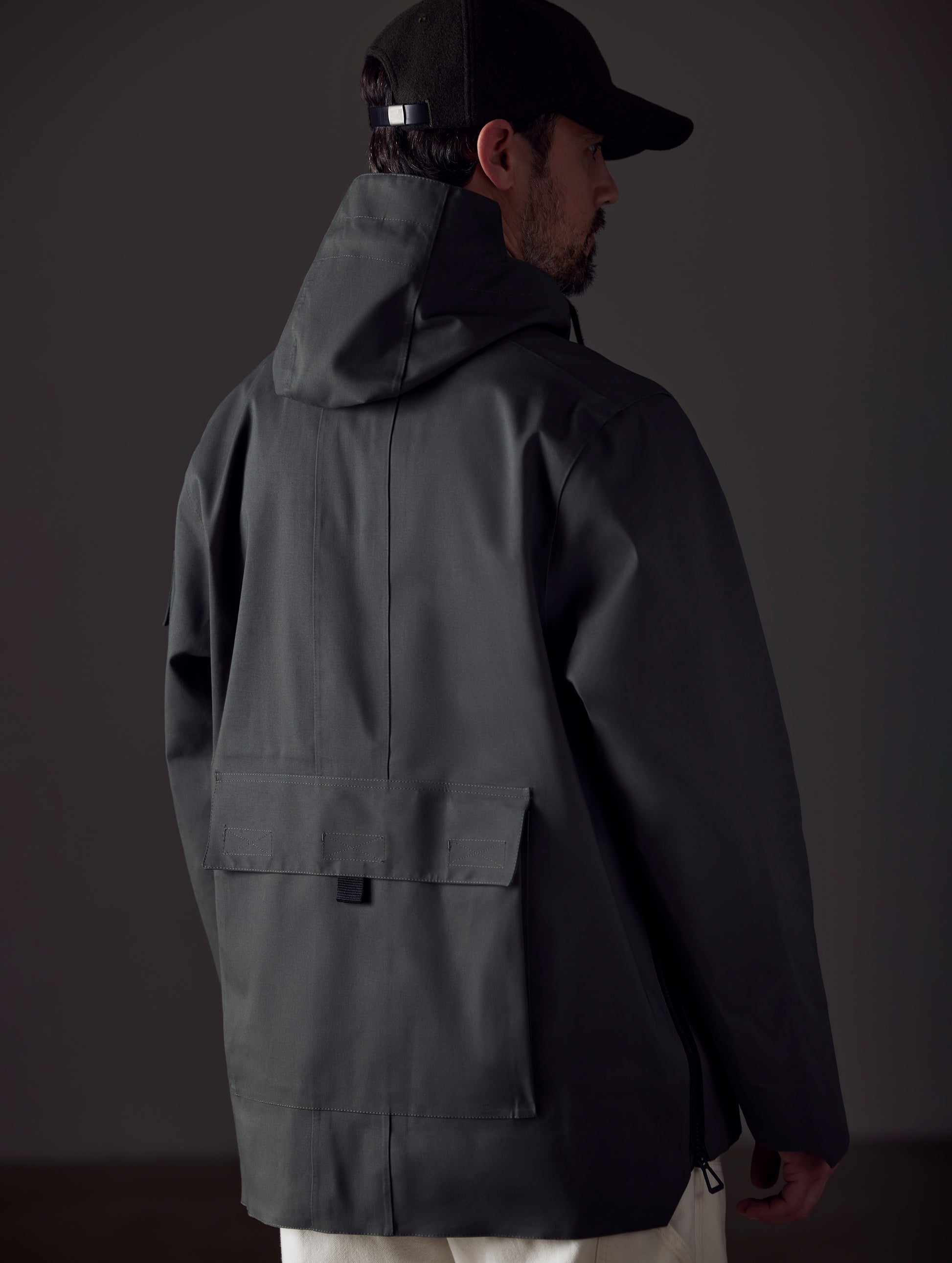 Rear 3/4 body view of man wearing AETHER + Mackintosh Field Anorak in Dark Bottle black.