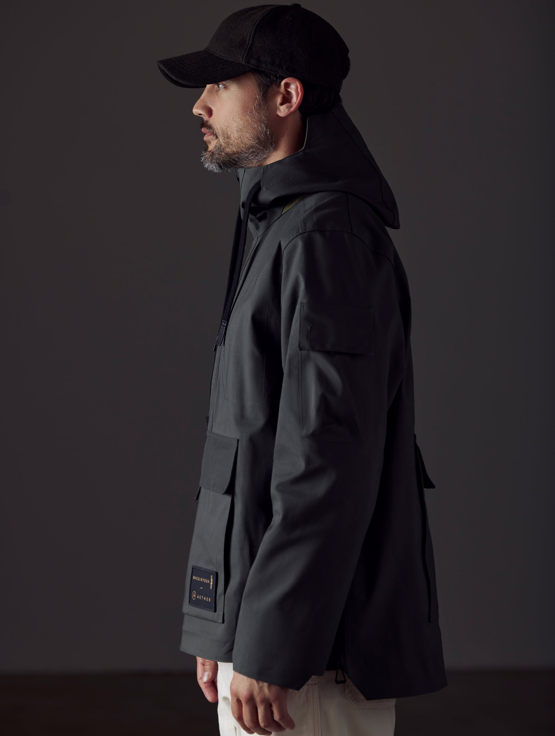 Side profile body view of man wearing AETHER + Mackintosh Field Anorak in Dark Bottle black.