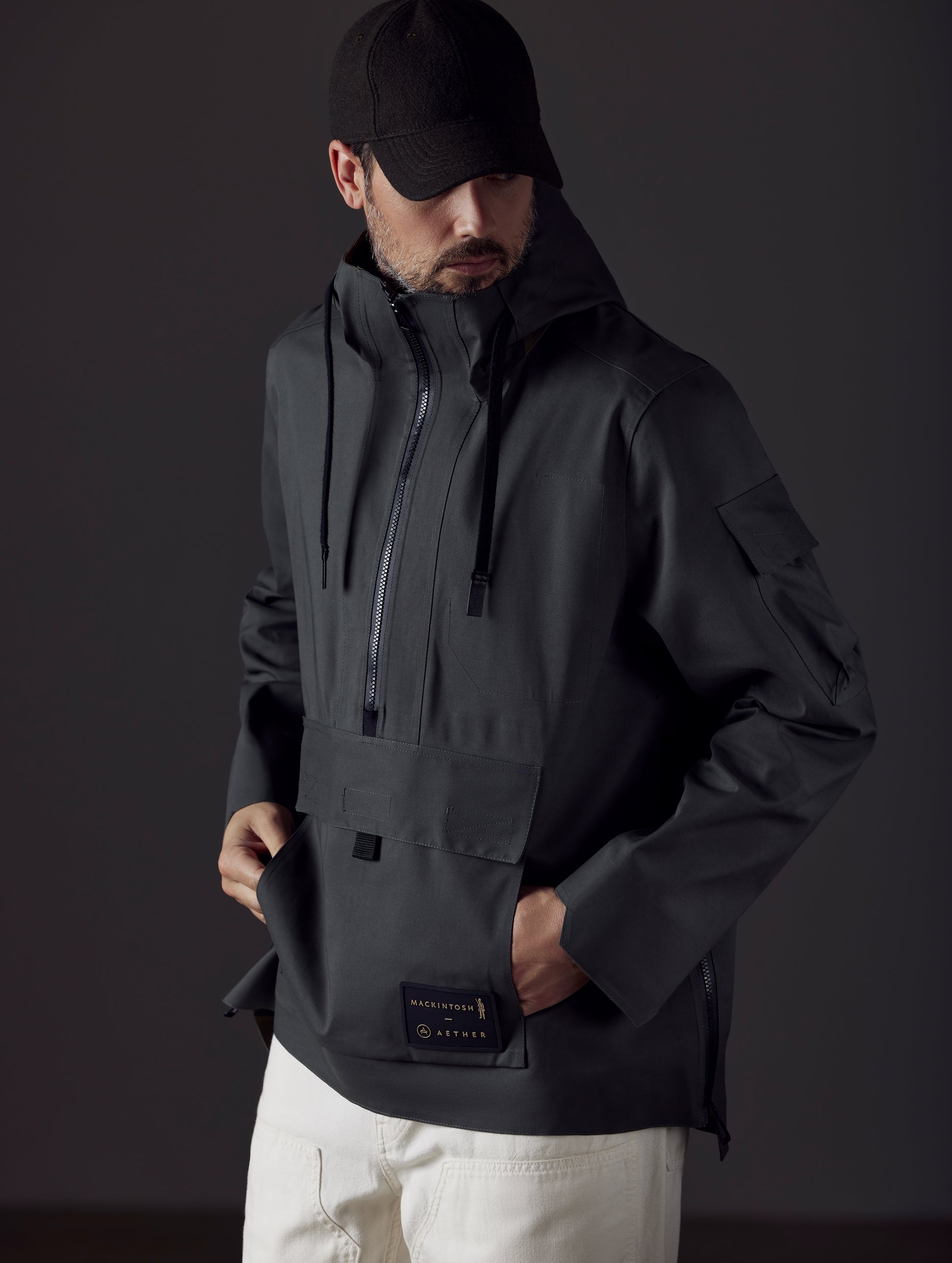 Front 3/4 body view of man wearing AETHER + Mackintosh Field Anorak in Dark Bottle black.