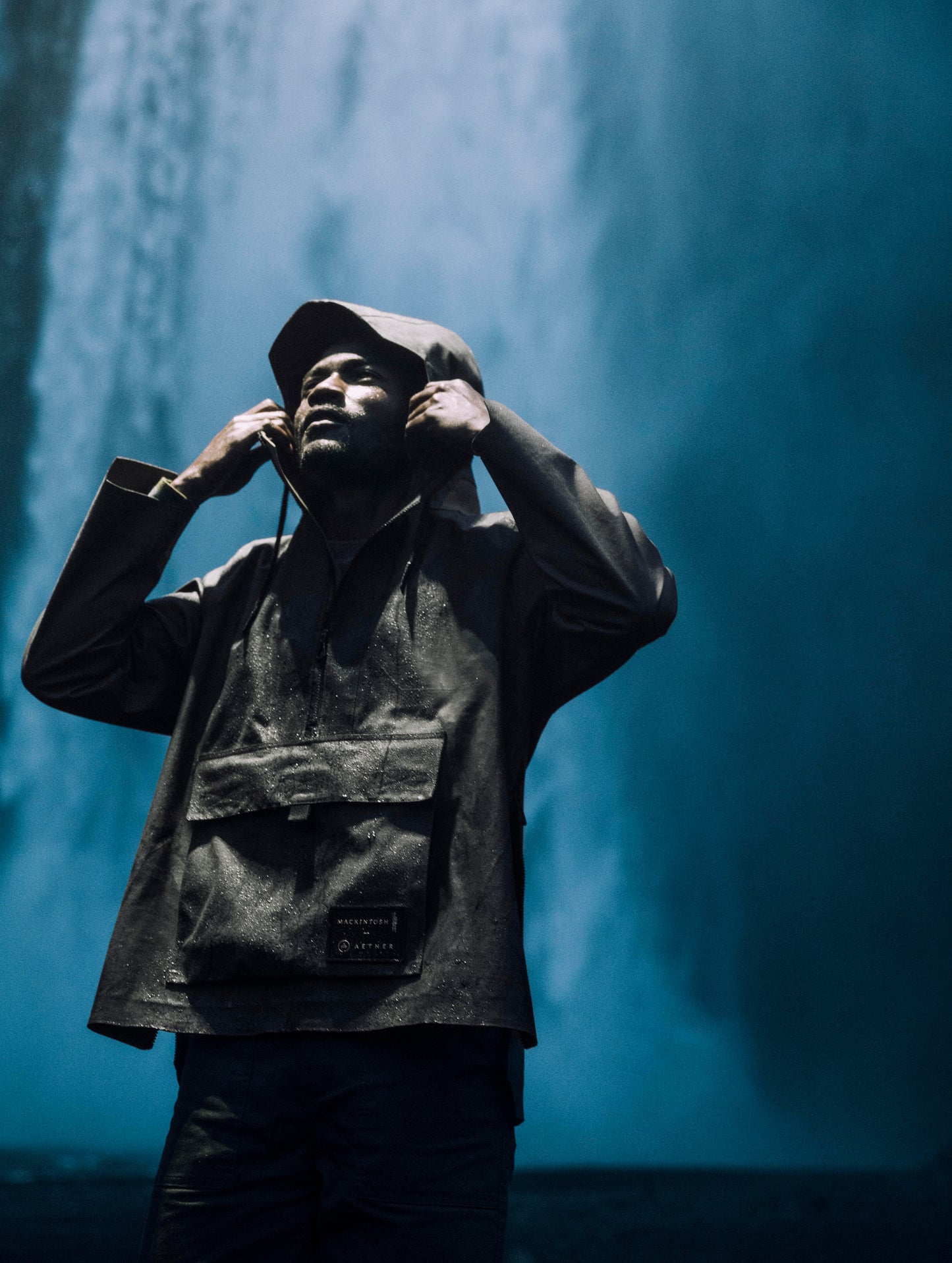 Man wearing dark green anorak in front of waterfall