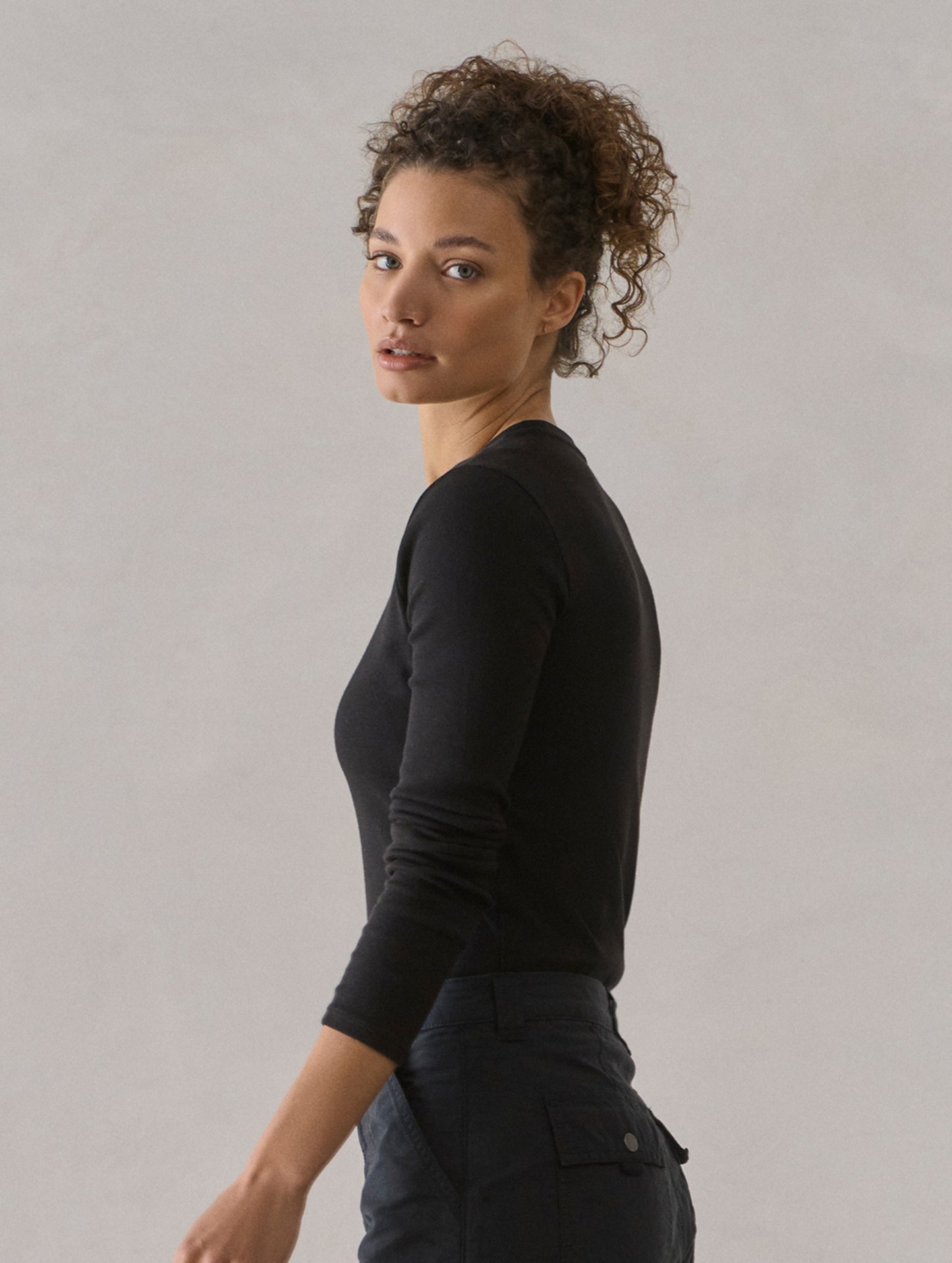 Side profile view of woman wearing Amara Long-Sleeve Crew in Onyx Black from AETHER Apparel.