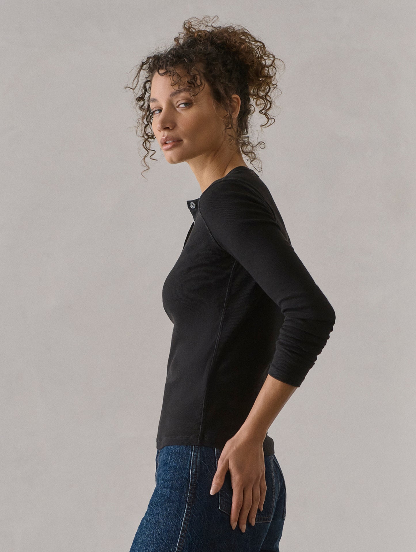 Side profile view of woman wearing Amara Long-Sleeve Ribbed Henley in Onyx Black from AETHER Apparel.