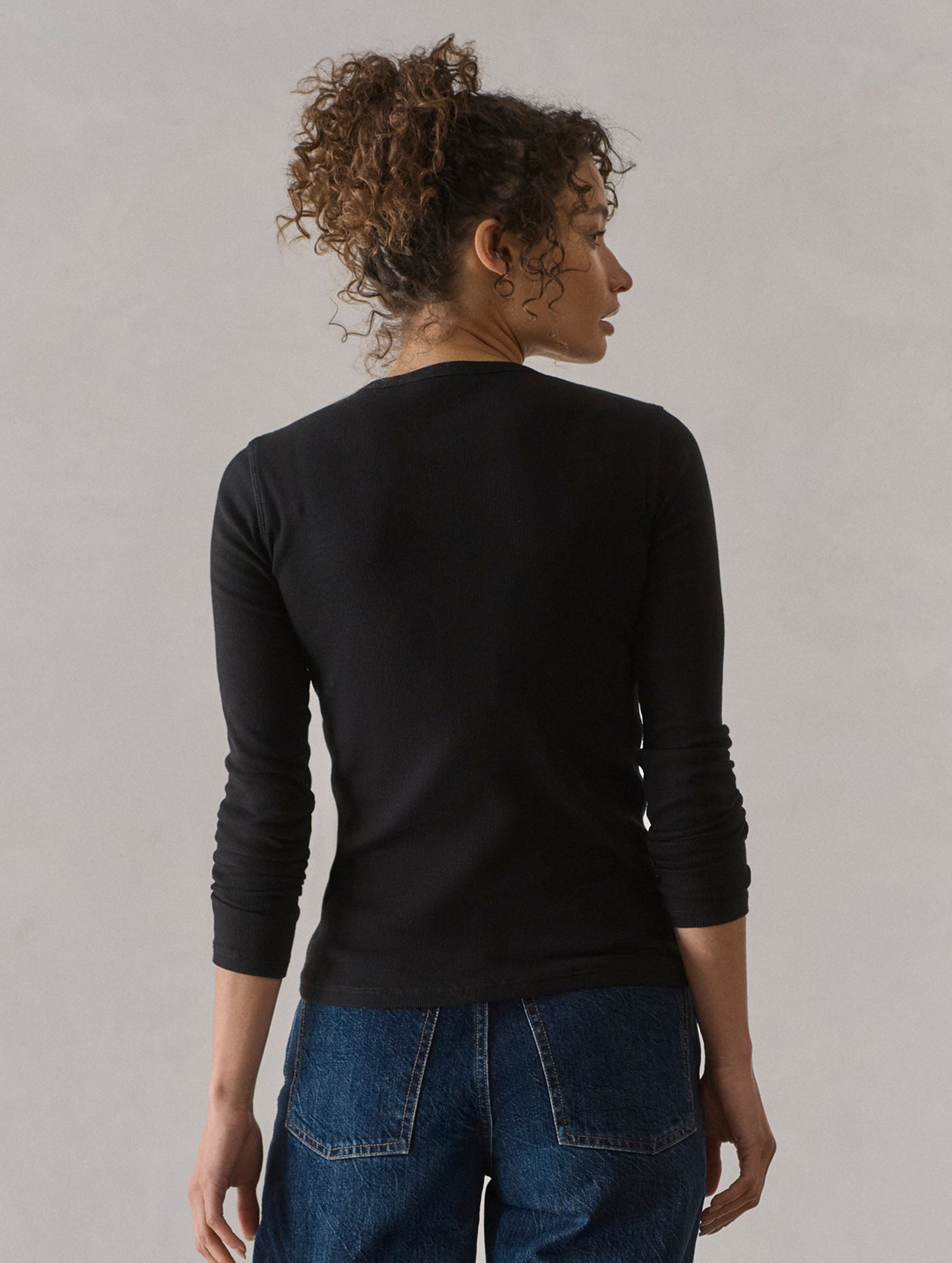 Rear view of woman wearing Amara Long-Sleeve Ribbed Henley in Onyx Black from AETHER Apparel.