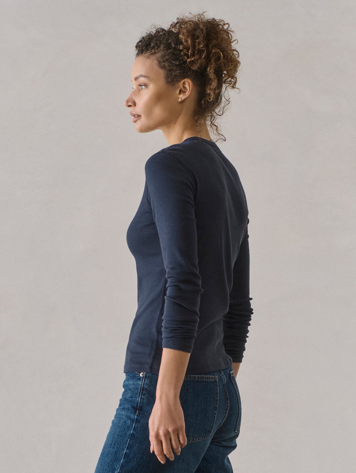 Side profile view of woman wearing Amara Long-Sleeve Ribbed Henley in Total Eclipse dark blue from AETHER Apparel.