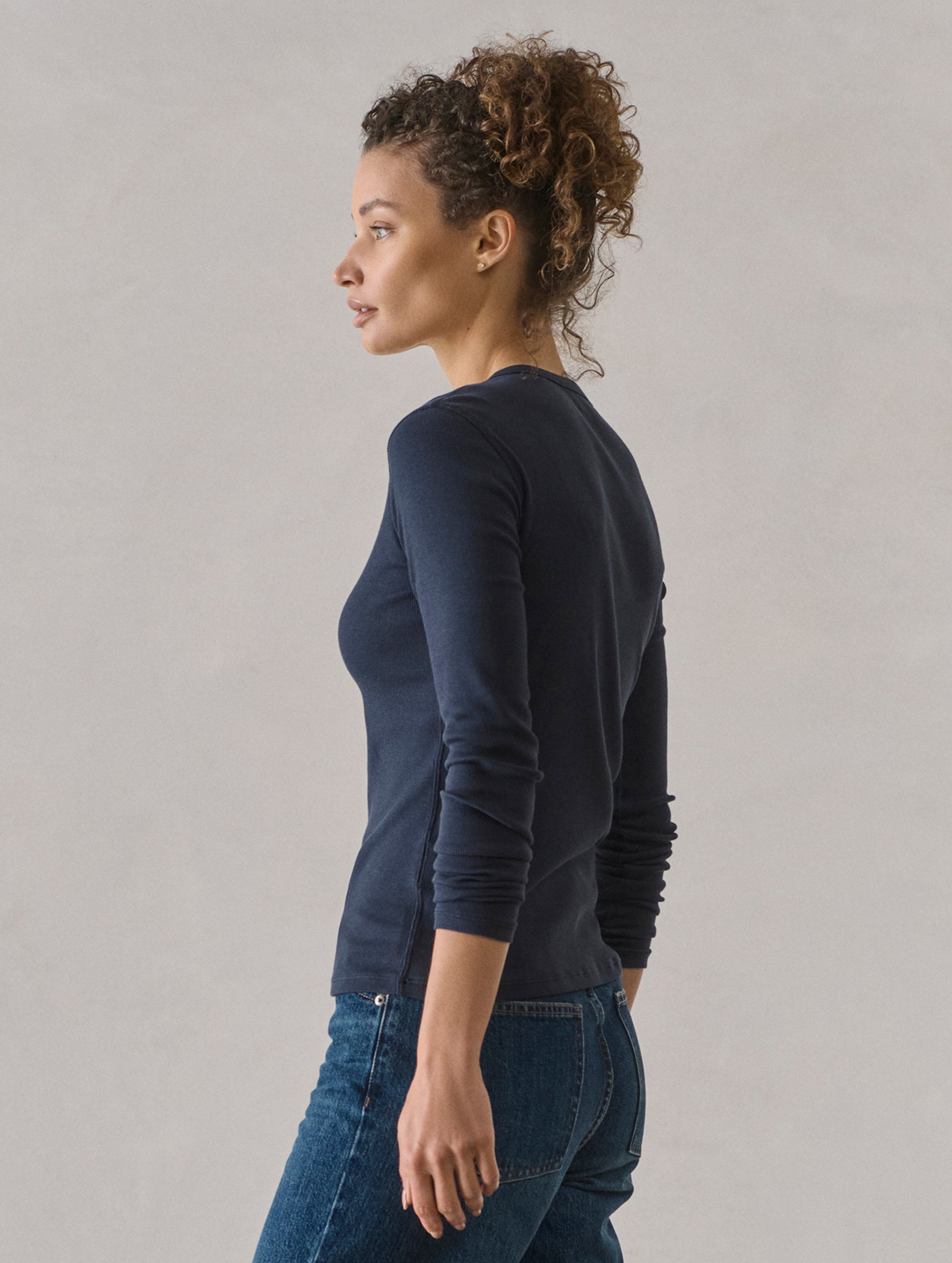Side profile view of woman wearing Amara Long-Sleeve Ribbed Henley in Total Eclipse dark blue from AETHER Apparel.