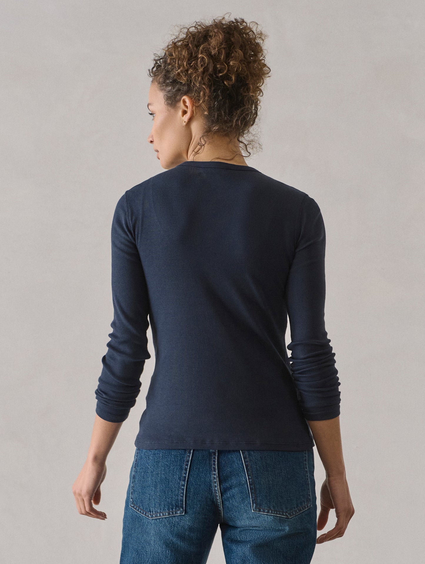 Rear view of woman wearing Amara Long-Sleeve Ribbed Henley in Total Eclipse dark blue from AETHER Apparel.