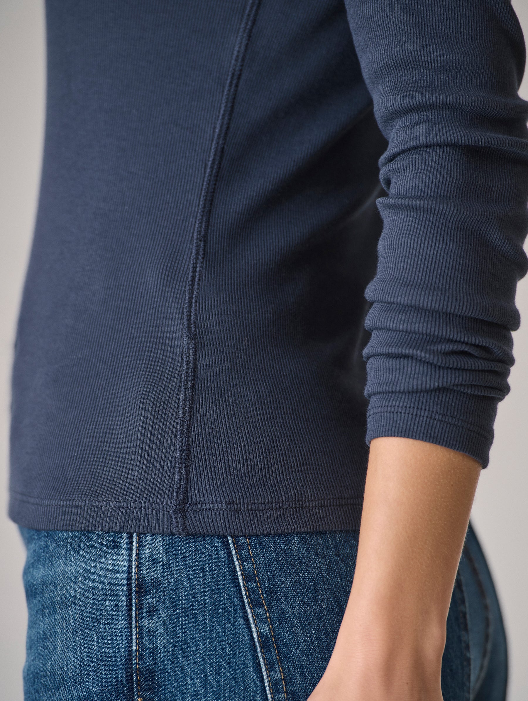 Closeup detailed view of the side seam coverstitching details on the Amara Long-Sleeve Ribbed Henley in Total Eclipse dark blue from AETHER Apparel.