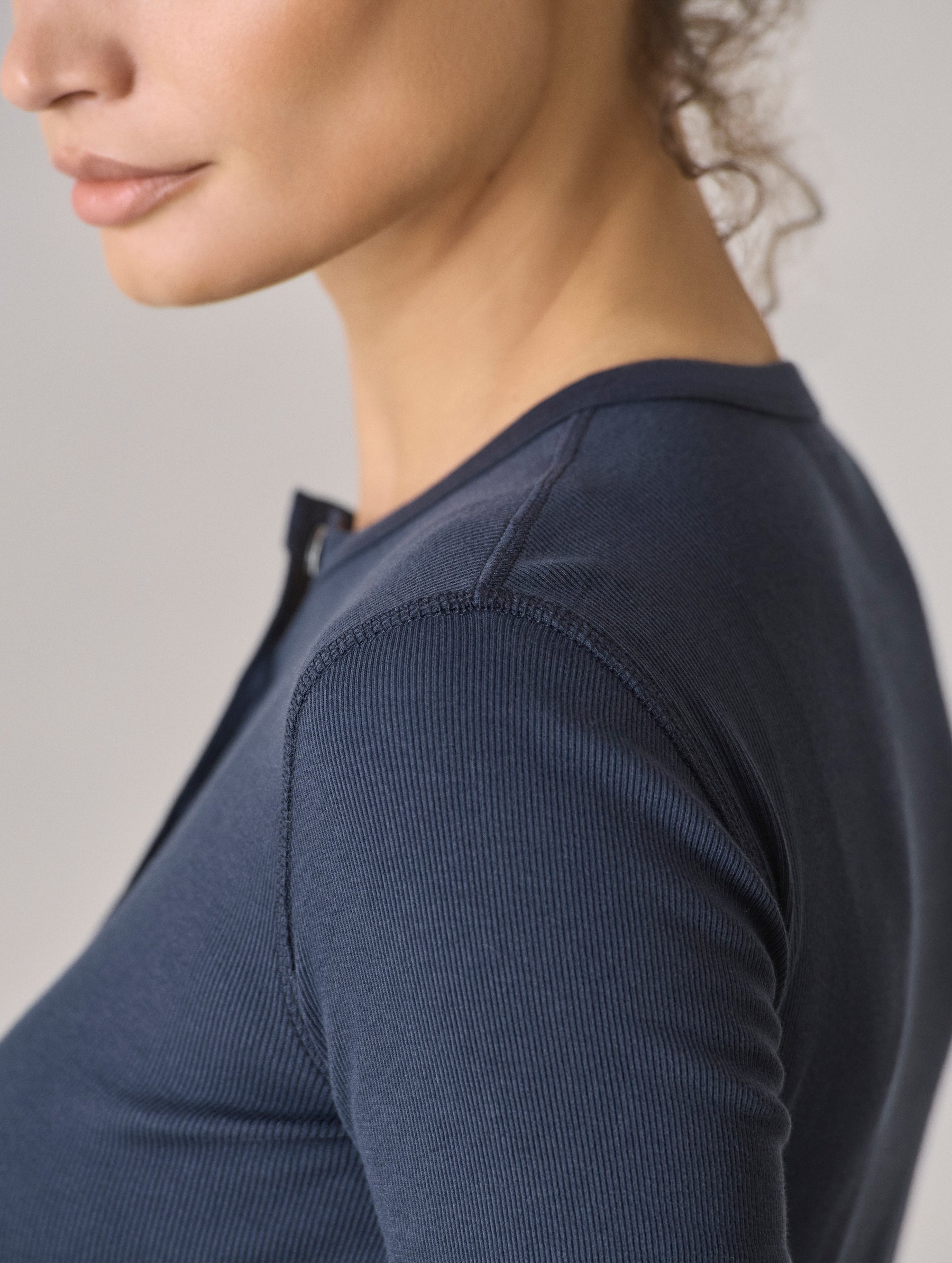 Closeup detailed view of the jersey binding at the neck opening and coverstitching details at the side seams on the Amara Long-Sleeve Ribbed Henley in Total Eclipse dark blue from AETHER Apparel.