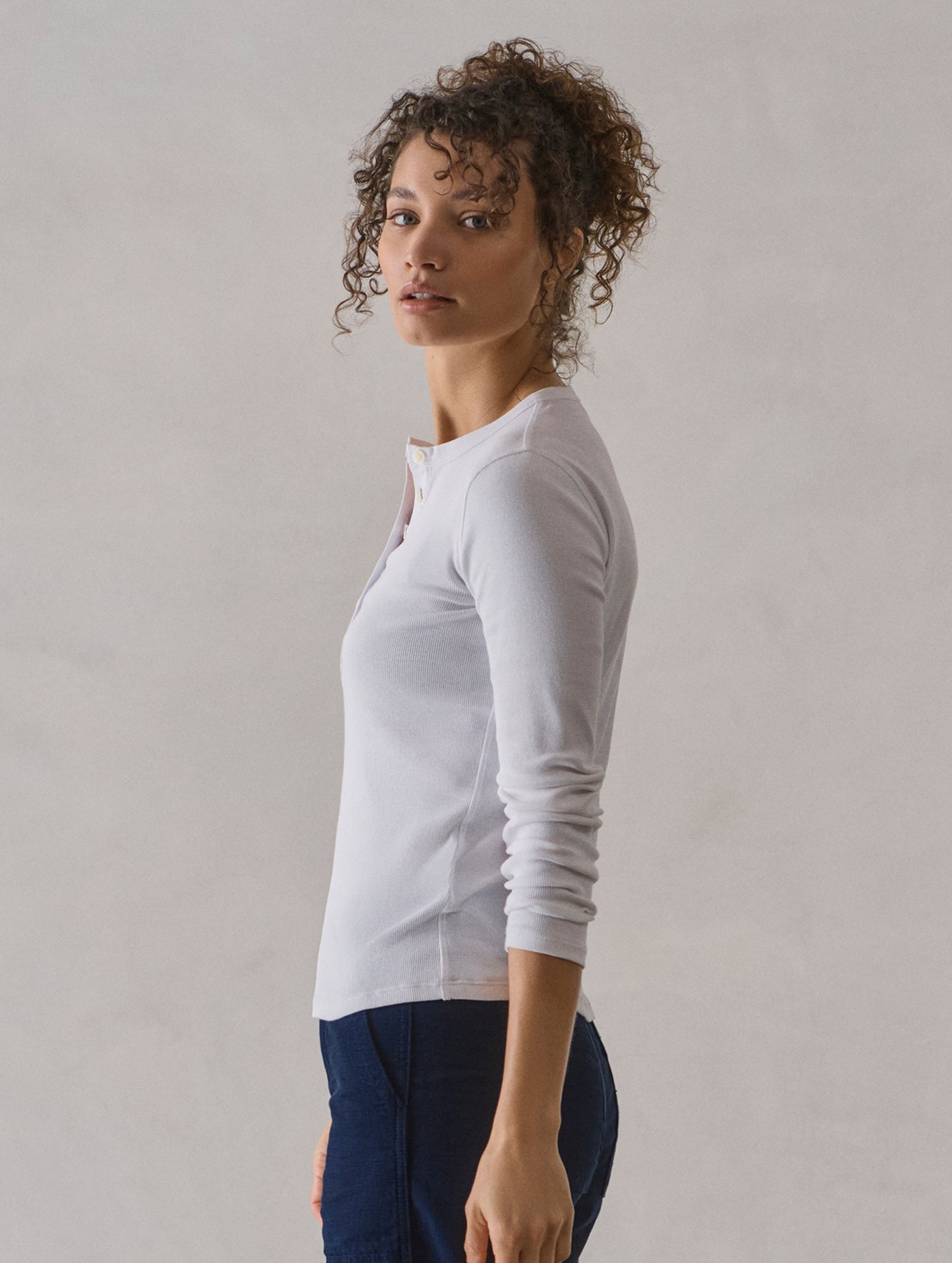 Side profile view of woman wearing Amara Long-Sleeve Ribbed Henley in White from AETHER Apparel.