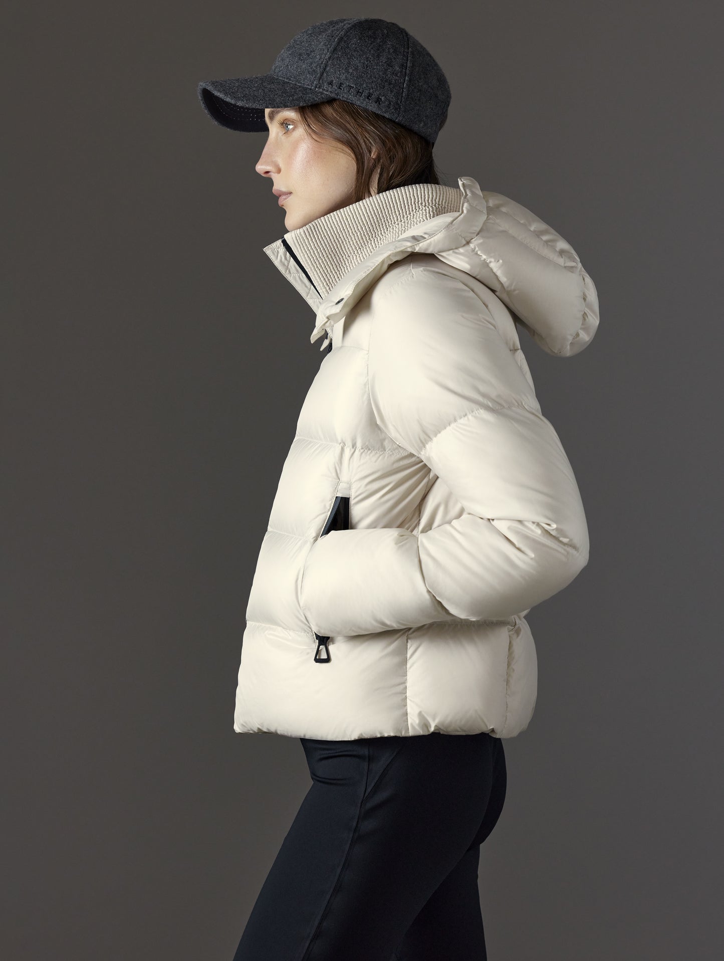 Side profile view of woman wearing Aura Puffer Jacket in Bone white from AETHER Apparel.