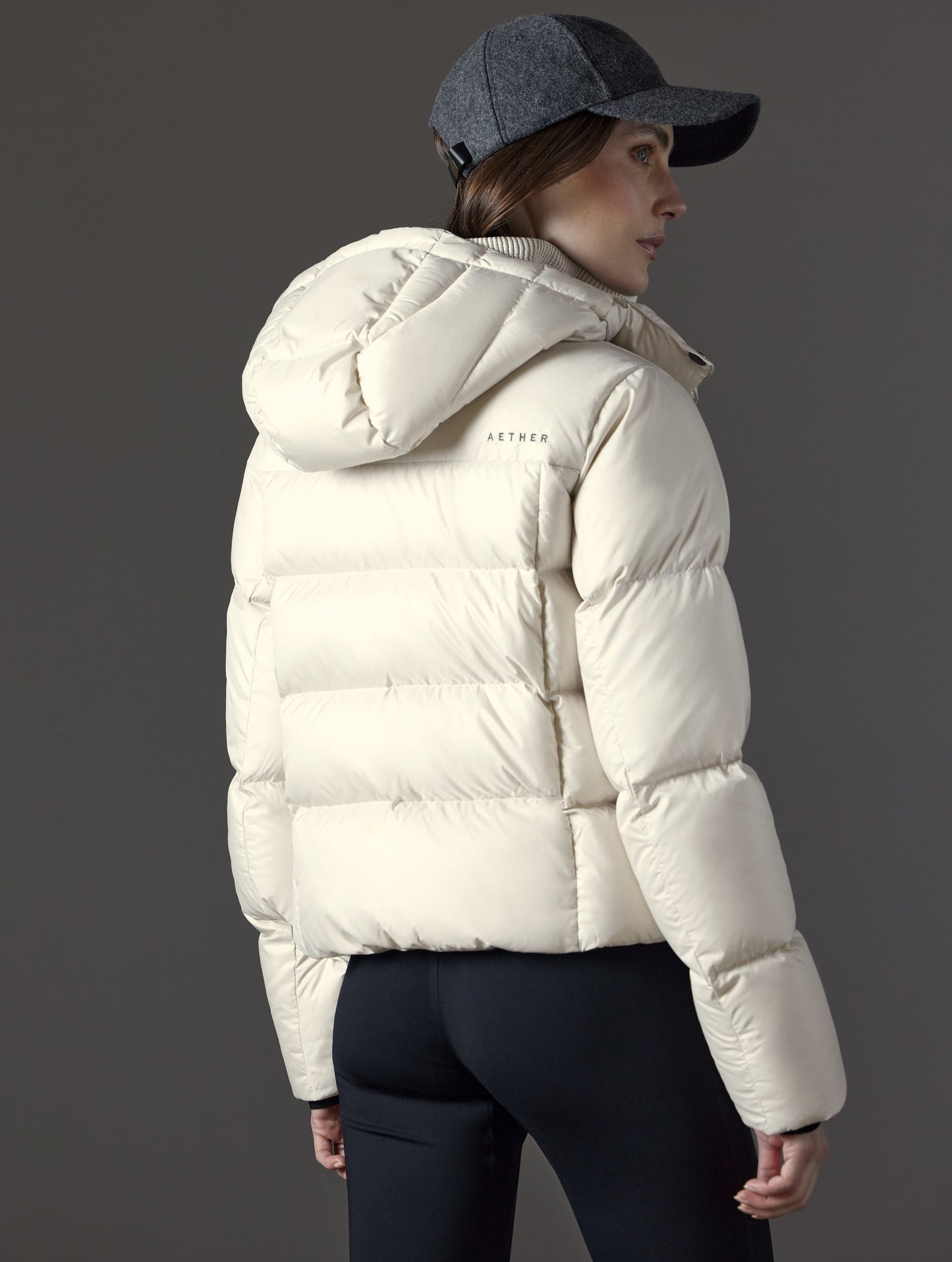 Rear angled view of woman wearing Aura Puffer Jacket in Bone white from AETHER Apparel.