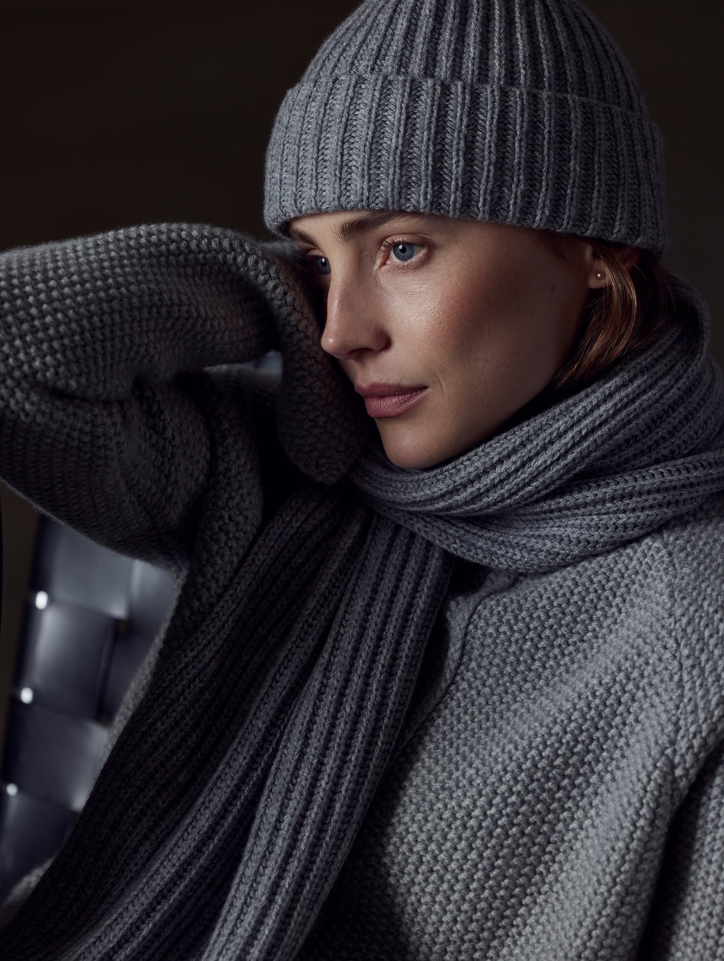 Closeup view of woman sitting in chair wearing Ribbed Cashmere Scarf in Heather Grey from AETHER Apparel.