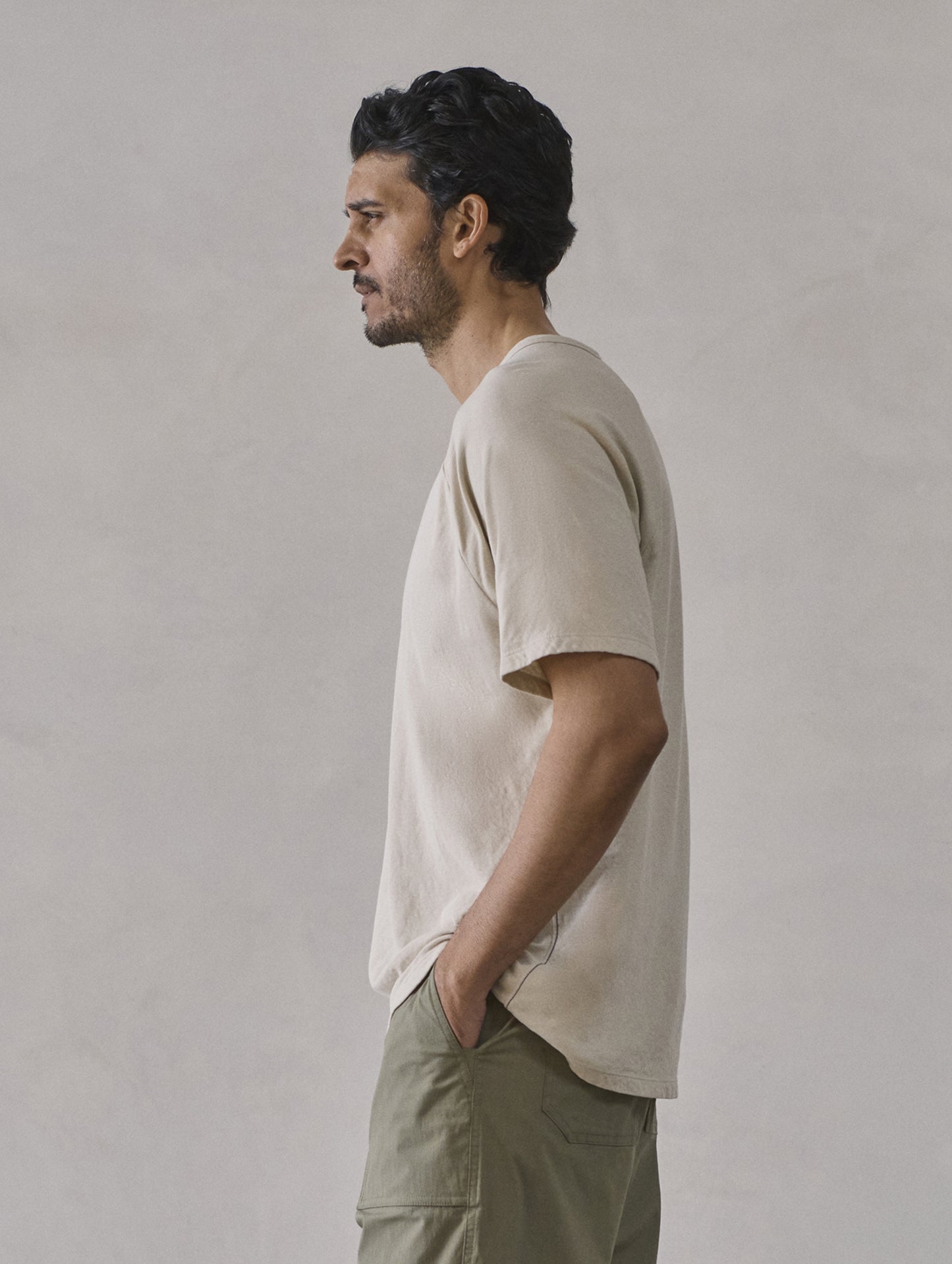 Left side profile upper-body view of man wearing Buckhorn Cotton Raglan Tee 2.0 in Bone white from AETHER Apparel.