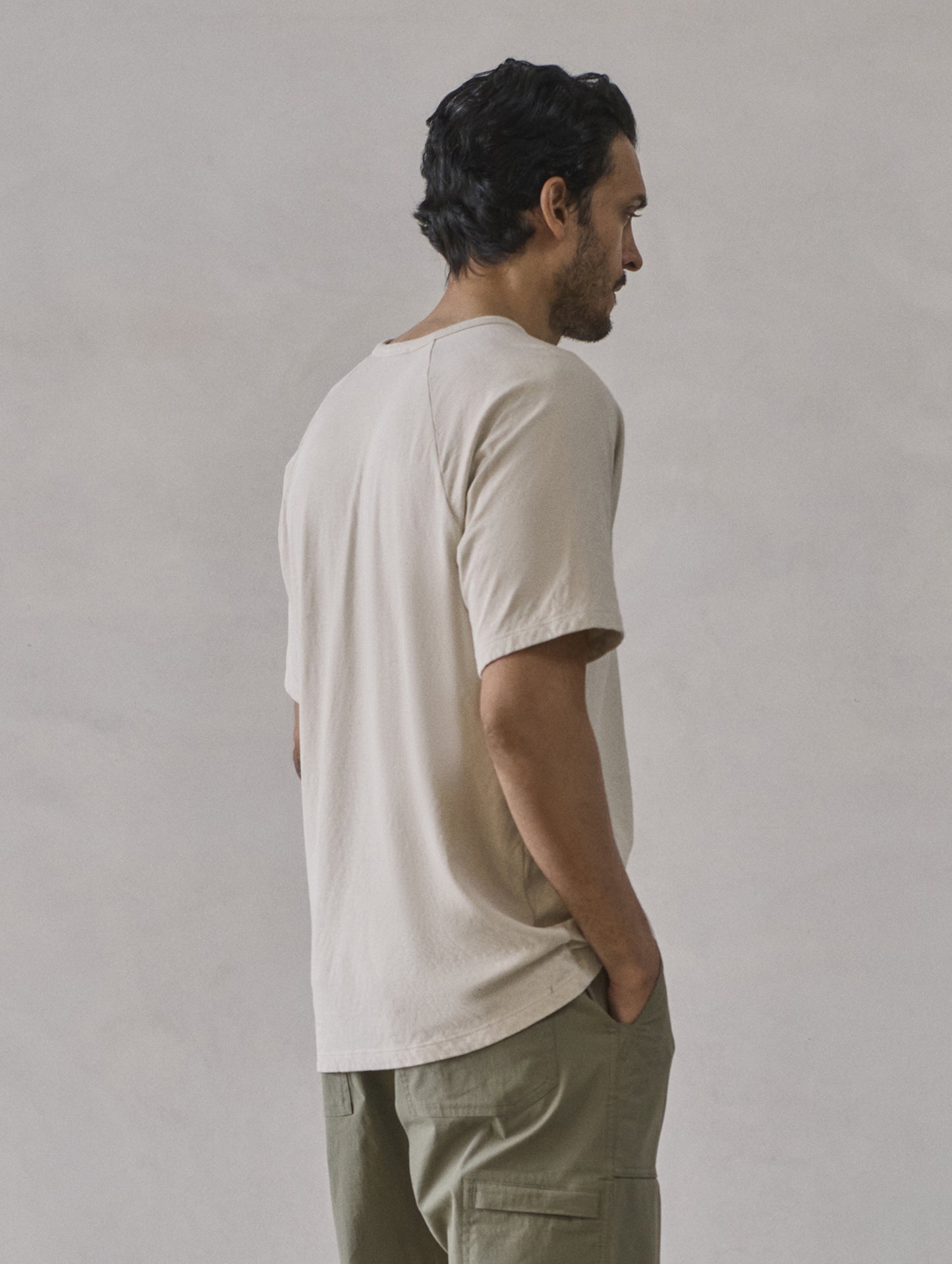 Rear 3/4 upper-body view of man wearing Buckhorn Cotton Raglan Tee 2.0 in Bone white from AETHER Apparel.