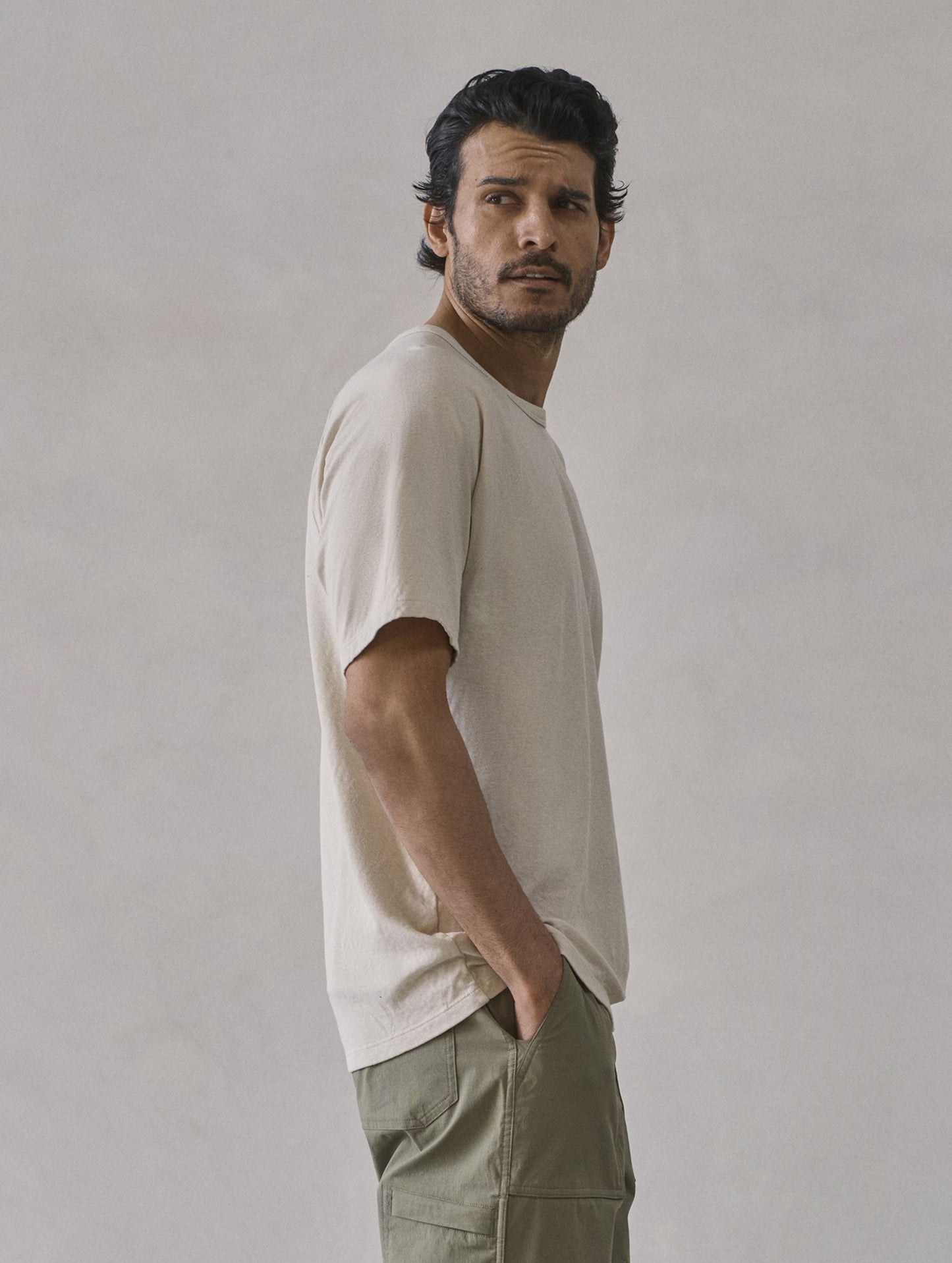 Right side profile upper-body view of man looking over shoulder wearing Buckhorn Cotton Raglan Tee 2.0 in Bone white from AETHER Apparel.