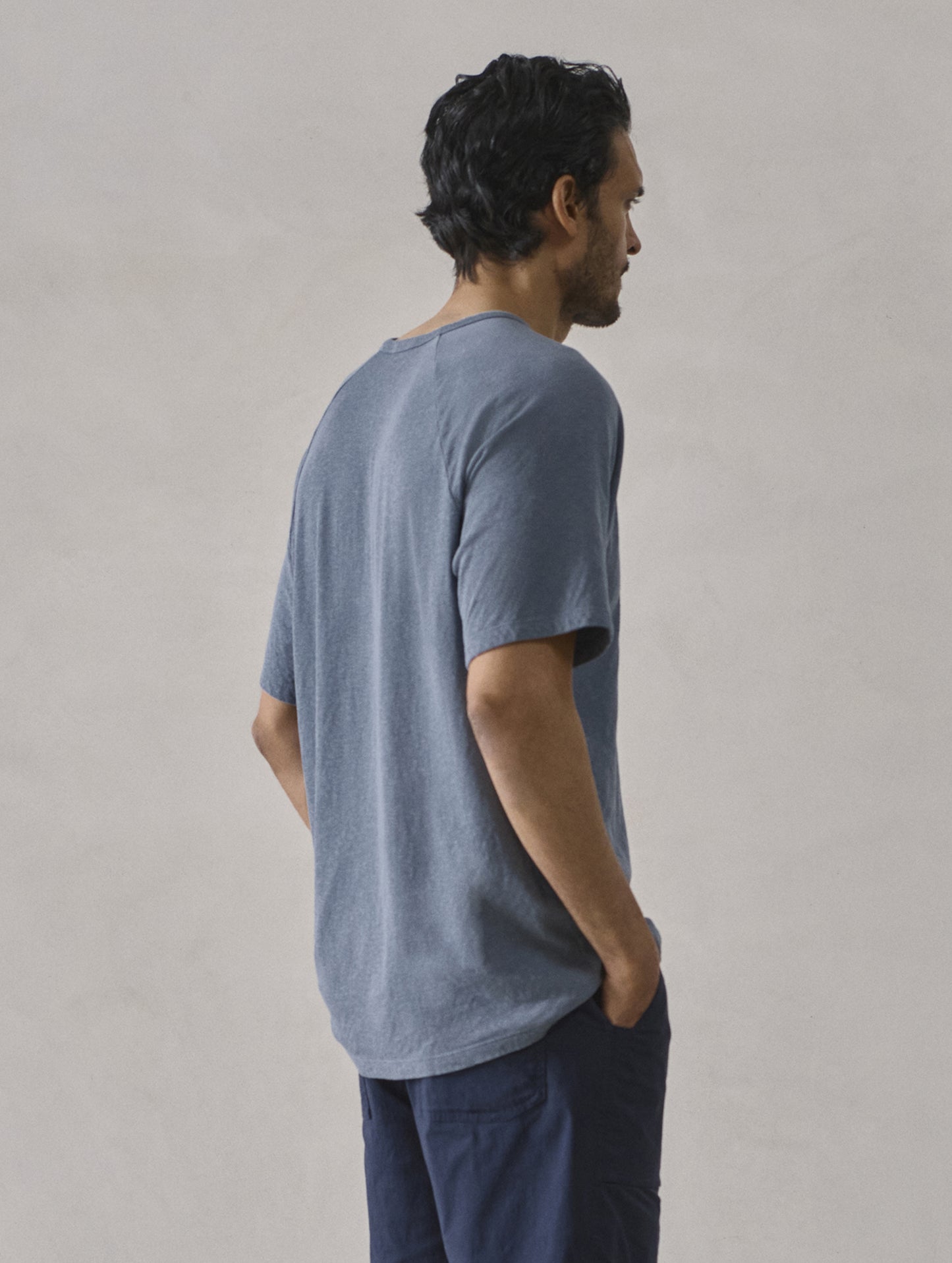 Rear 3/4 upper-body view of man wearing Buckhorn Cotton Raglan Tee 2.0 in Portal Blue from AETHER Apparel.