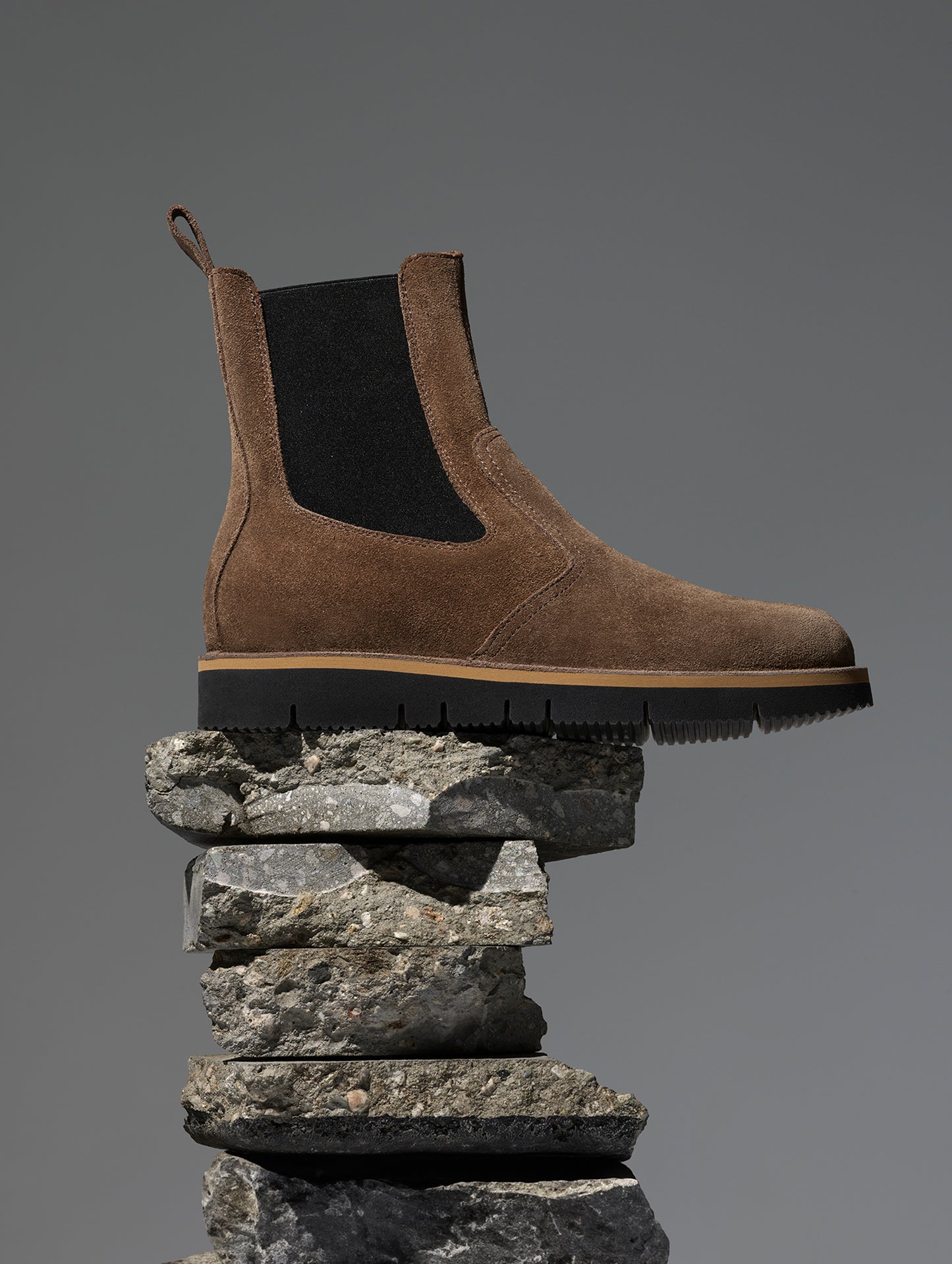 Studio side profile image of AETHER Chelsea Boot in Taupe from AETHER Apparel on pile of rocks.