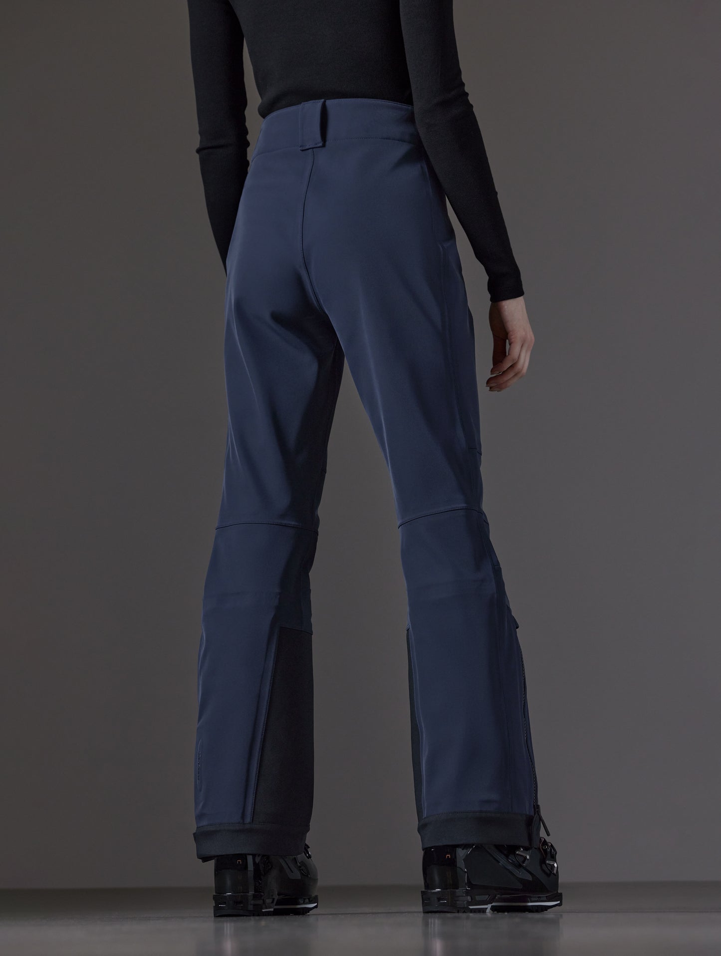 Rear angled lower body view of woman wearing Descent Pant in Total Eclipse dark blue from AETHER Apparel.
