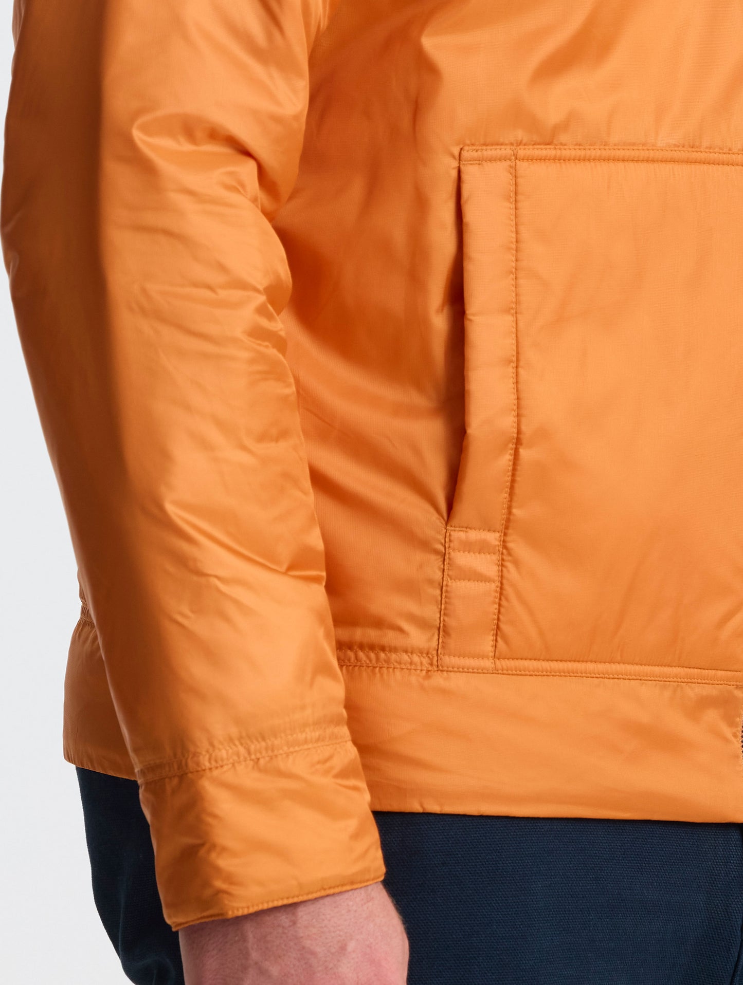 Closeup view of wearer's right hand pocket of Eco Space Hoodie in Autumn Orange from AETHER Apparel.