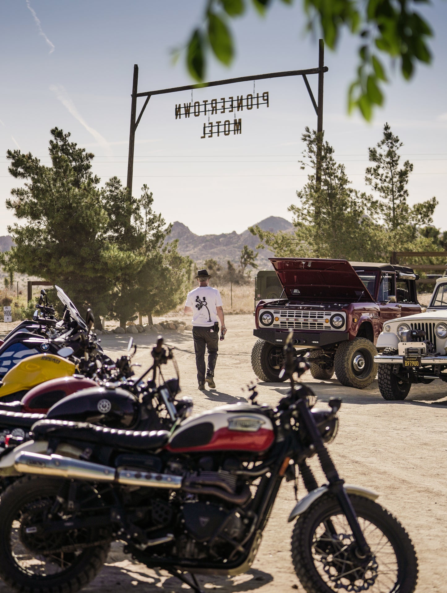 Image of motorcycles and cars lined up in front of the main gate at the Pioneertown Motel for the at the AETHER Pioneertown Rally.