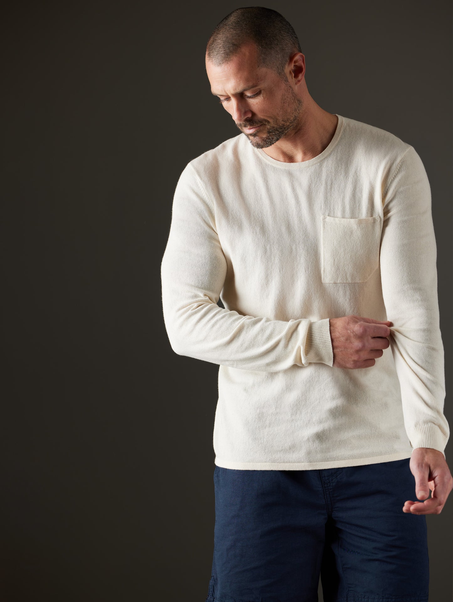 Front body view of man pulling on sleeve of Aero Sweater in Oatmeal Heather from AETHER Apparel.