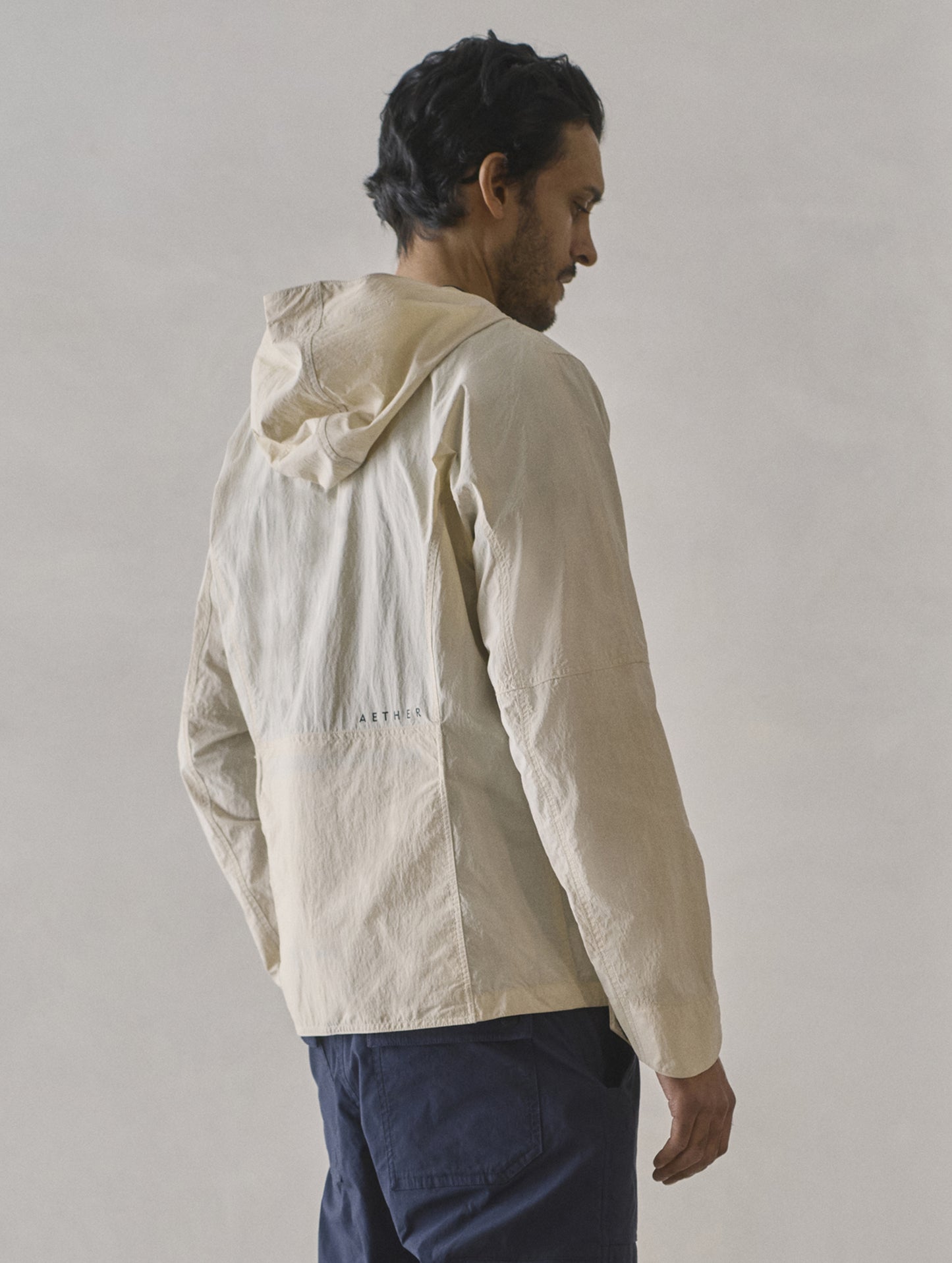 Rear 3/4 body view of man wearing Aires Lightweight Windbreaker in Bone white from AETHER Apparel.