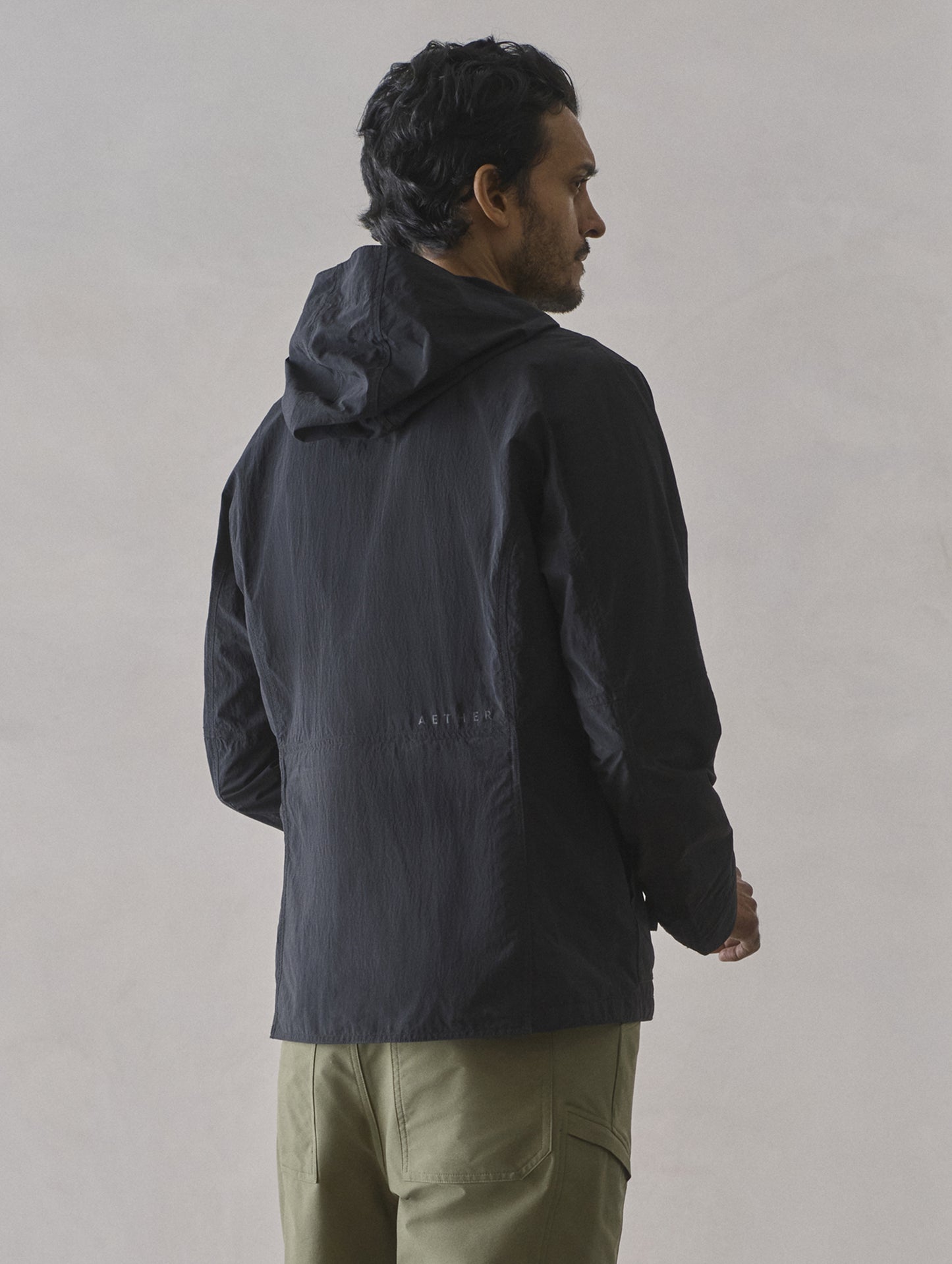 Rear 3/4 body view of man wearing Aires Lightweight Windbreaker in Onyx Black from AETHER Apparel.