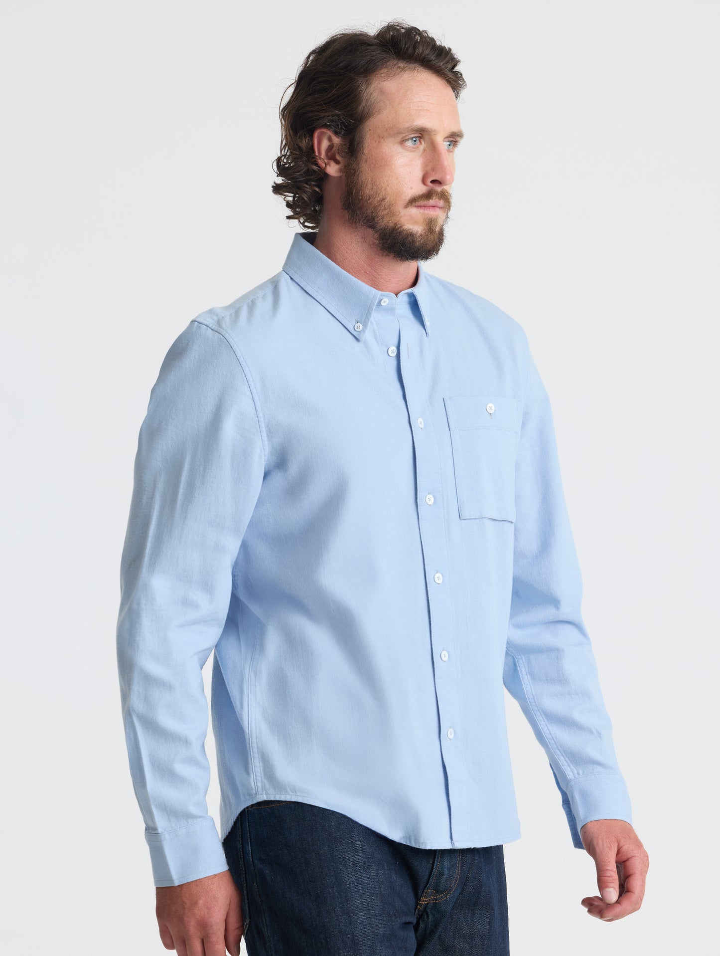 Angled view of man wearing Alder Chambray Button-Down in Light Blue from AETHER Apparel.