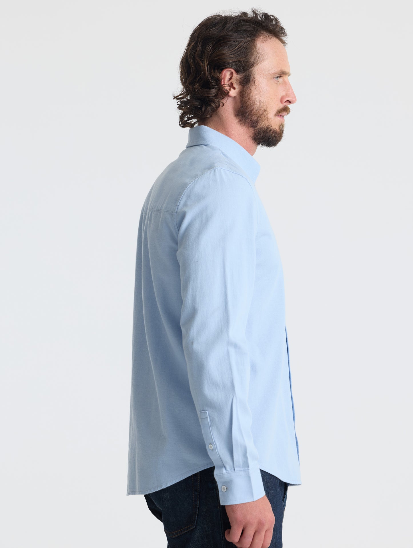 Right profile view of man wearing Alder Chambray Button-Down in Light Blue from AETHER Apparel.
