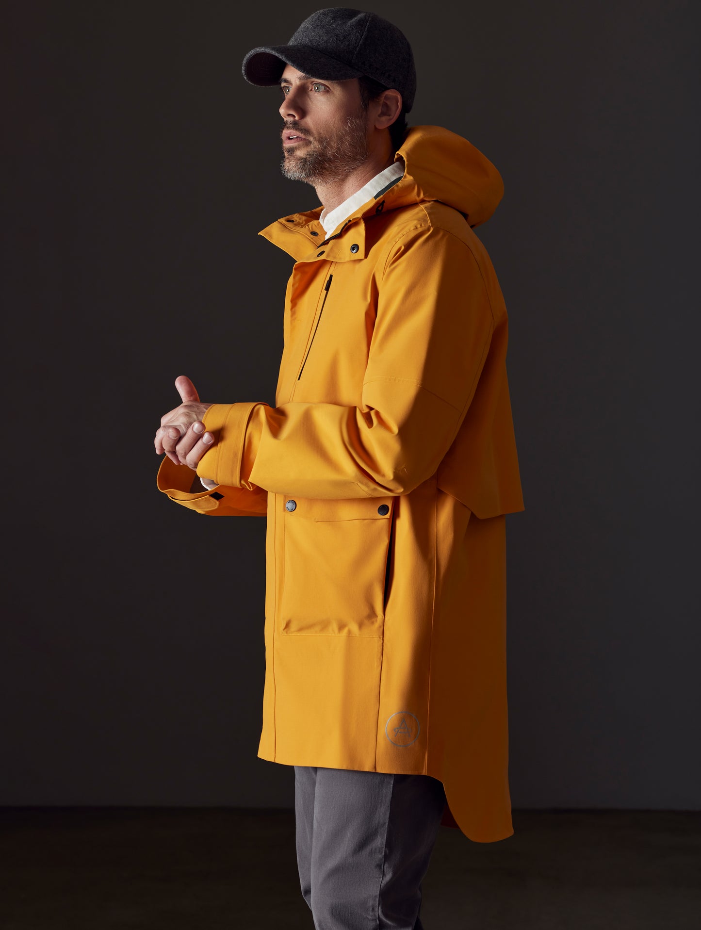 Side profile body view of man wearing Anders Rain Jacket in Midas Orange from AETHER Apparel.