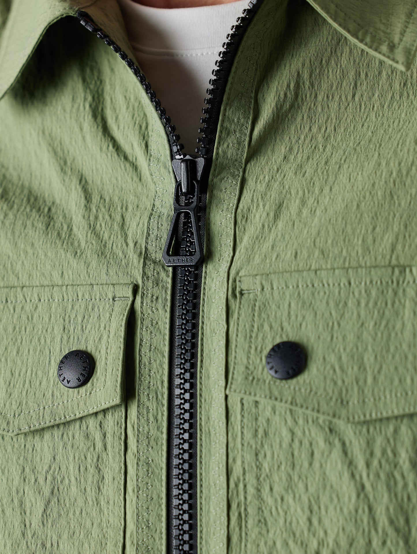 Close-up detailed view of main zipper, zipper pull, and chest pocket buttons on Baxter Jacket in Mineral Green from AETHER Apparel.