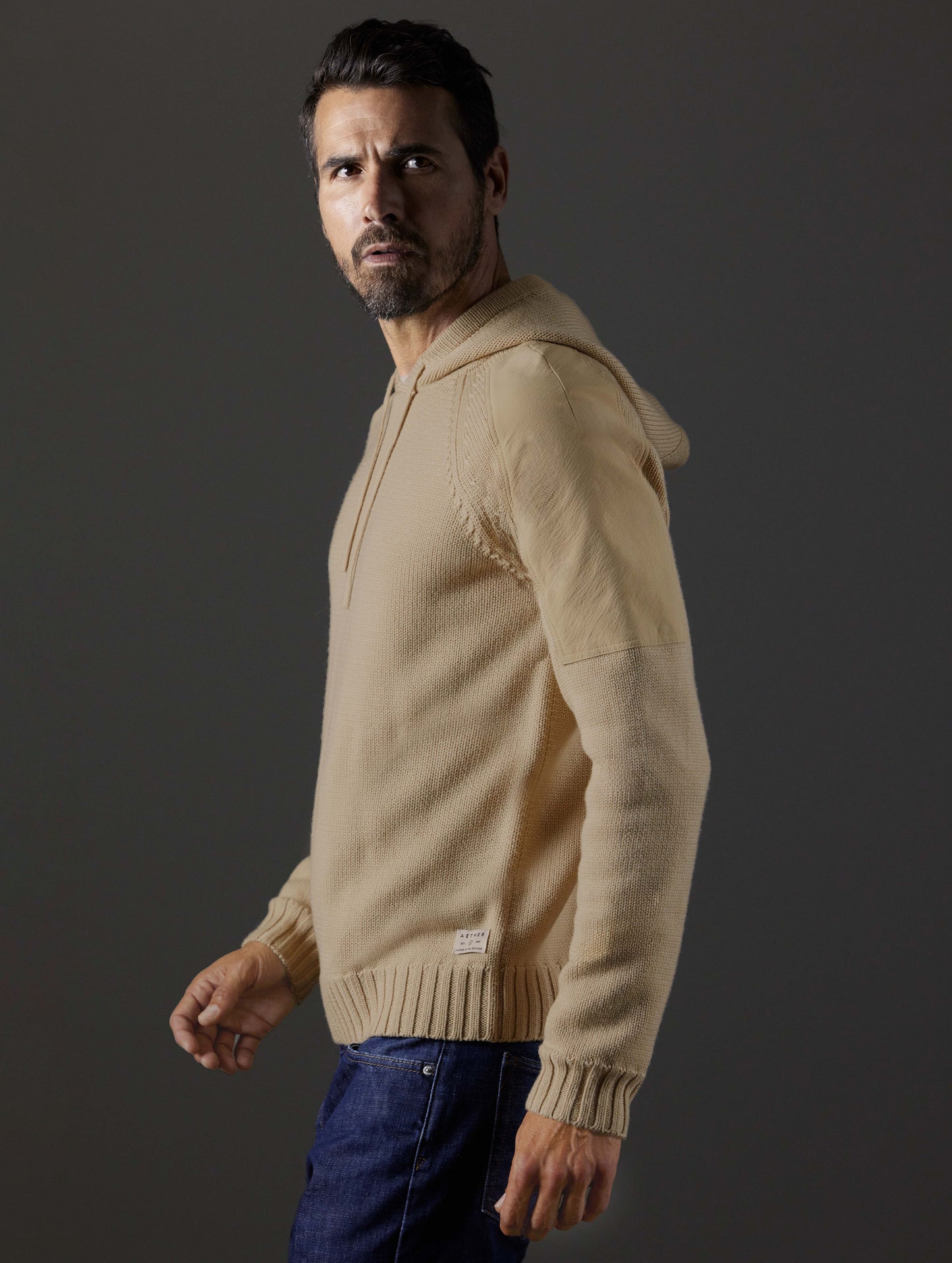 Side profile body view of man wearing Benson Hooded Sweater in Oatmeal beige from AETHER Apparel.
