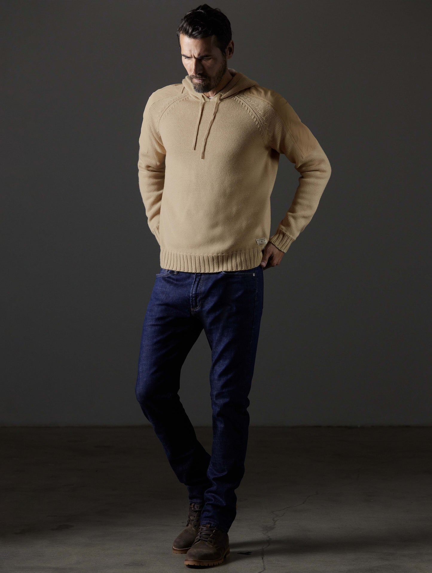 Front 3/4 full-body view of man wearing Benson Hooded Sweater in Oatmeal beige from AETHER Apparel.
