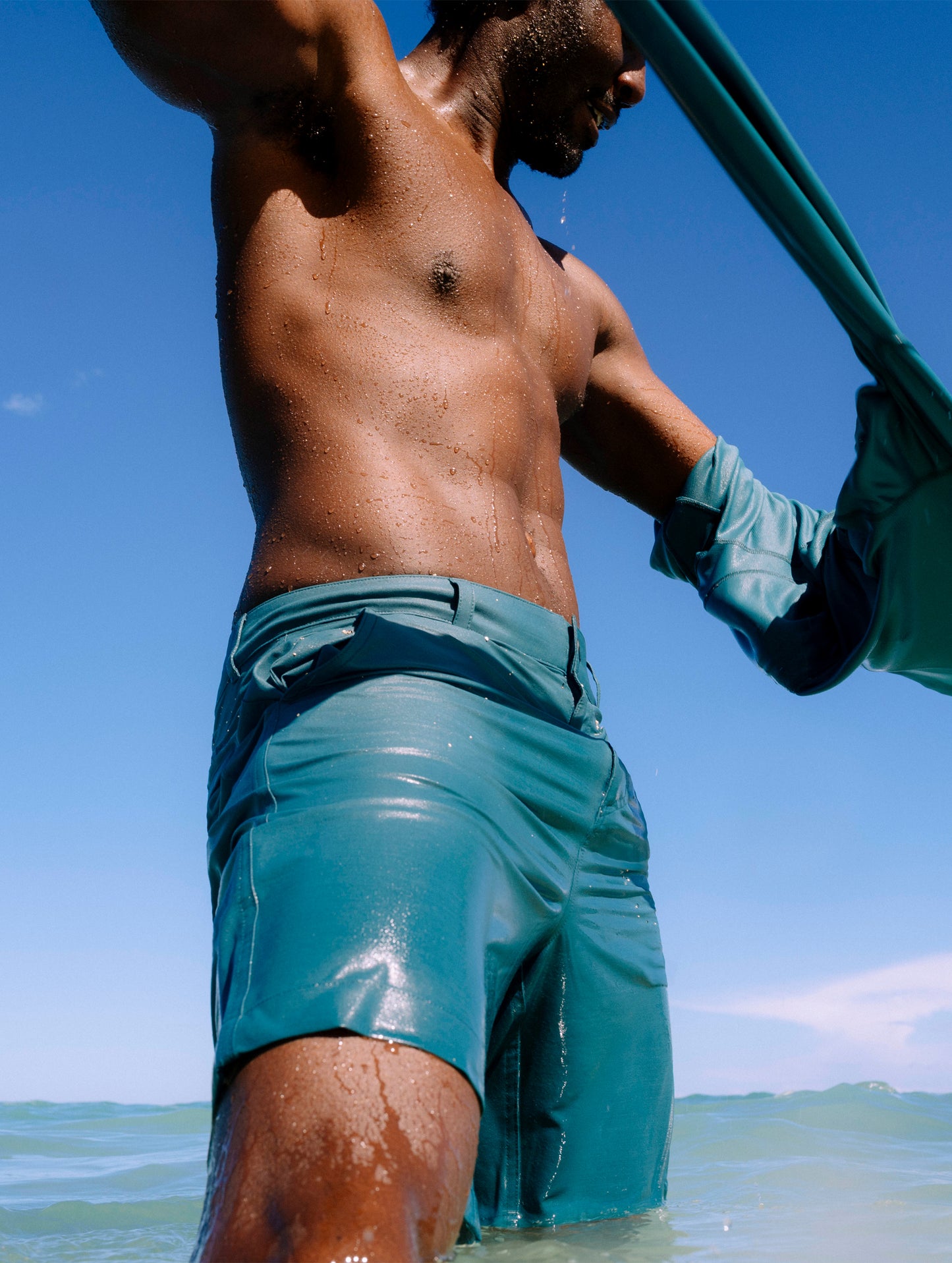 Lifestyle image of man standing in the ocean wearing Catalina Submersible Short in Aqua Blue from AETHER Apparel.
