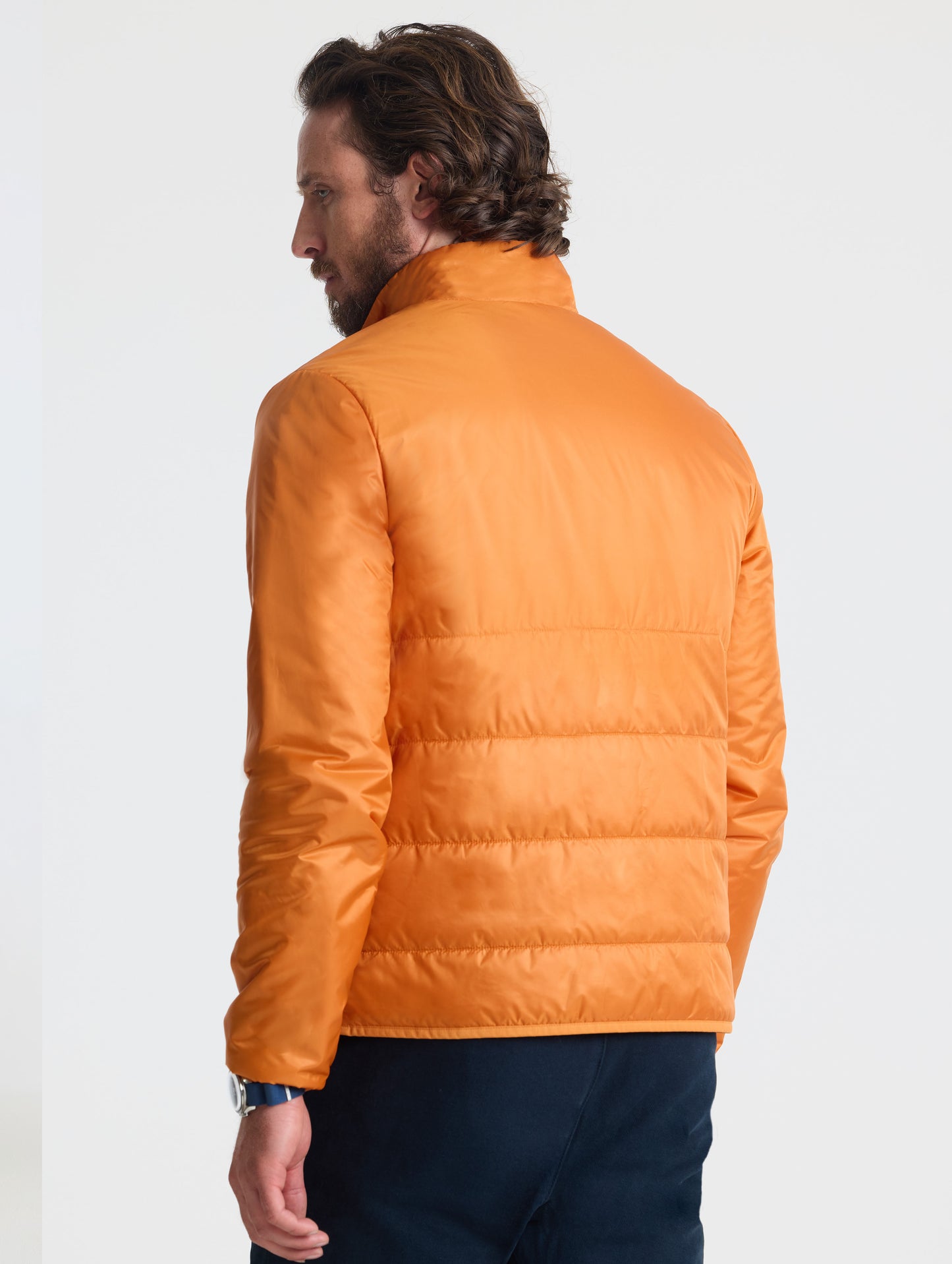 Rear angled view of man wearing Eco Insulated Jacket in Autumn Orange from AETHER Apparel.