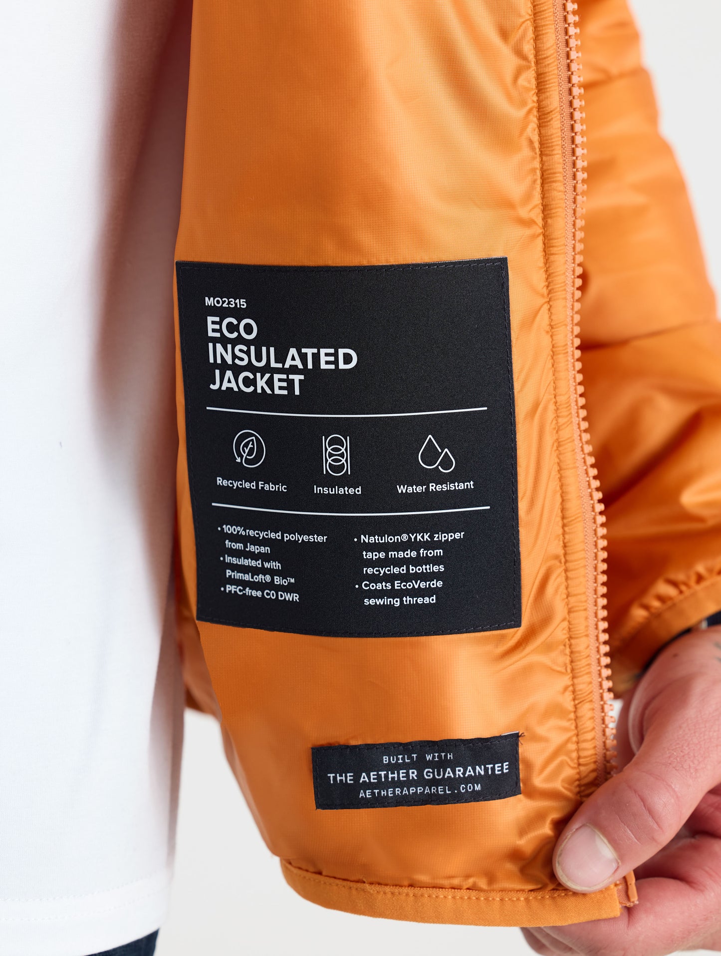 Closeup view of wearer's left interior label of Eco Insulated Jacket in Autumn Orange from AETHER Apparel.