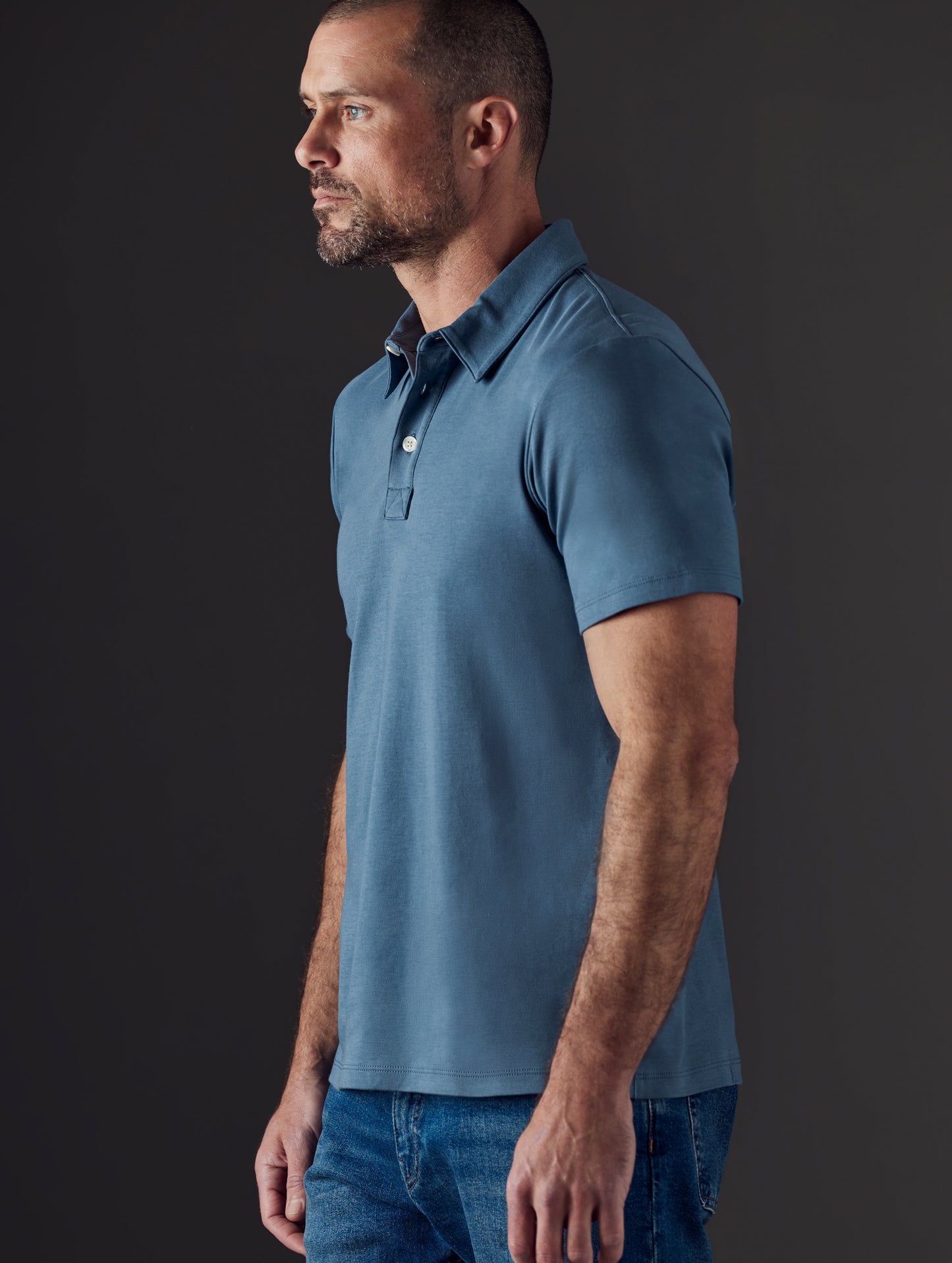 Side profile body view of man wearing Emery Pima Polo in Coastal Blue from AETHER Apparel.