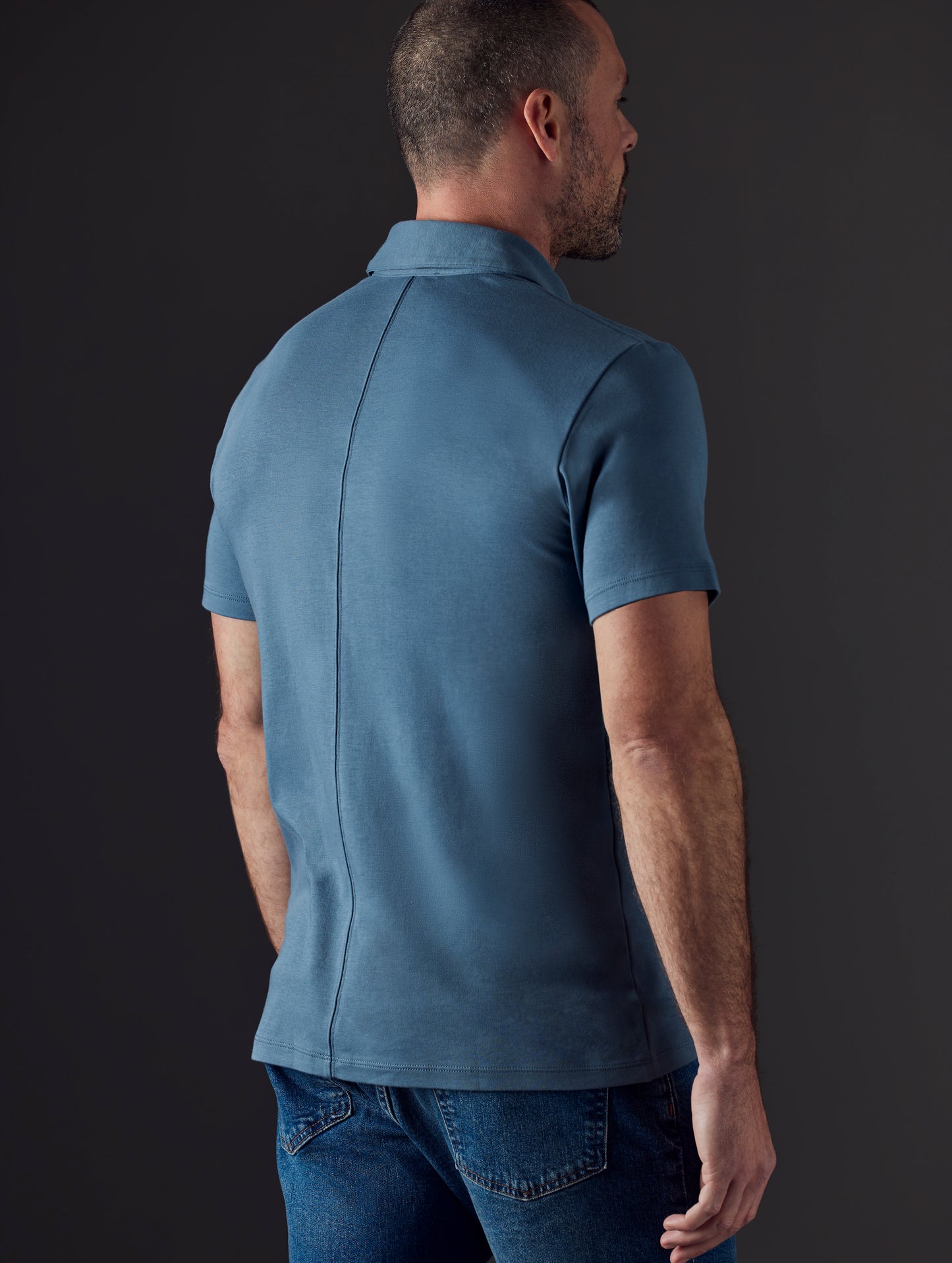 Rear 3/4 body view of man wearing Emery Pima Polo in Coastal Blue from AETHER Apparel.