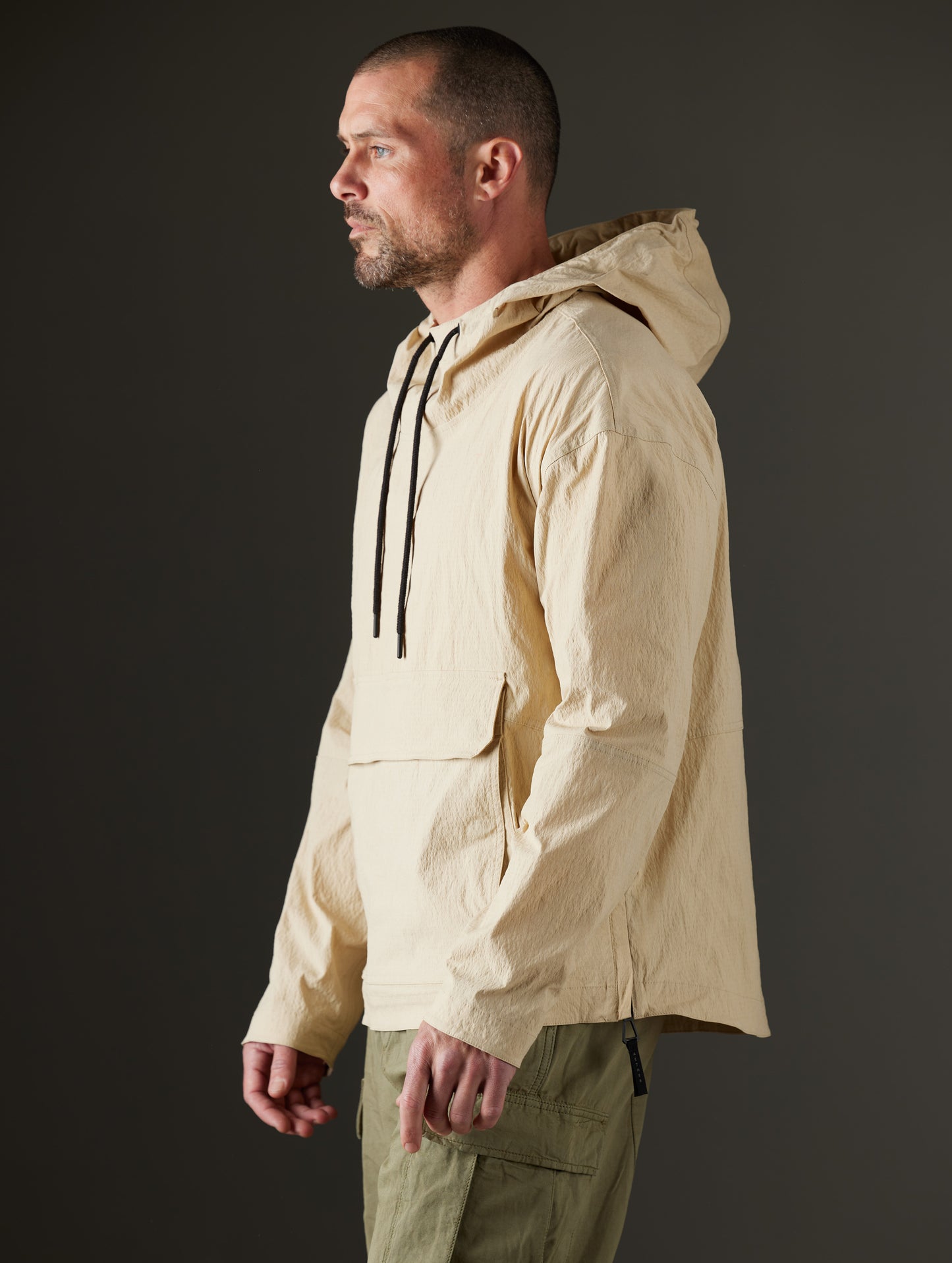 Side profile body view of man wearing Harrier Anorak in Desert Tan from AETHER Apparel.