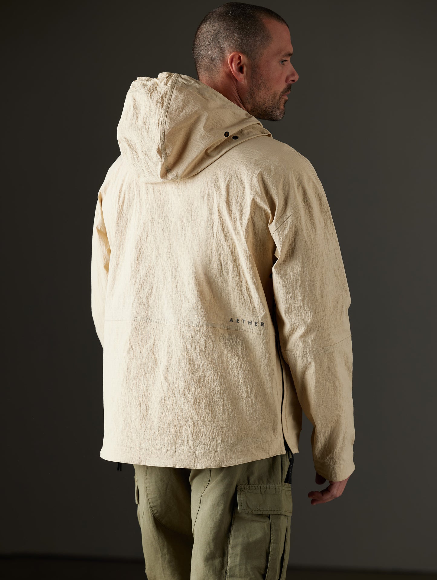 Rear 3/4 body view of man wearing Harrier Anorak in Desert Tan from AETHER Apparel.