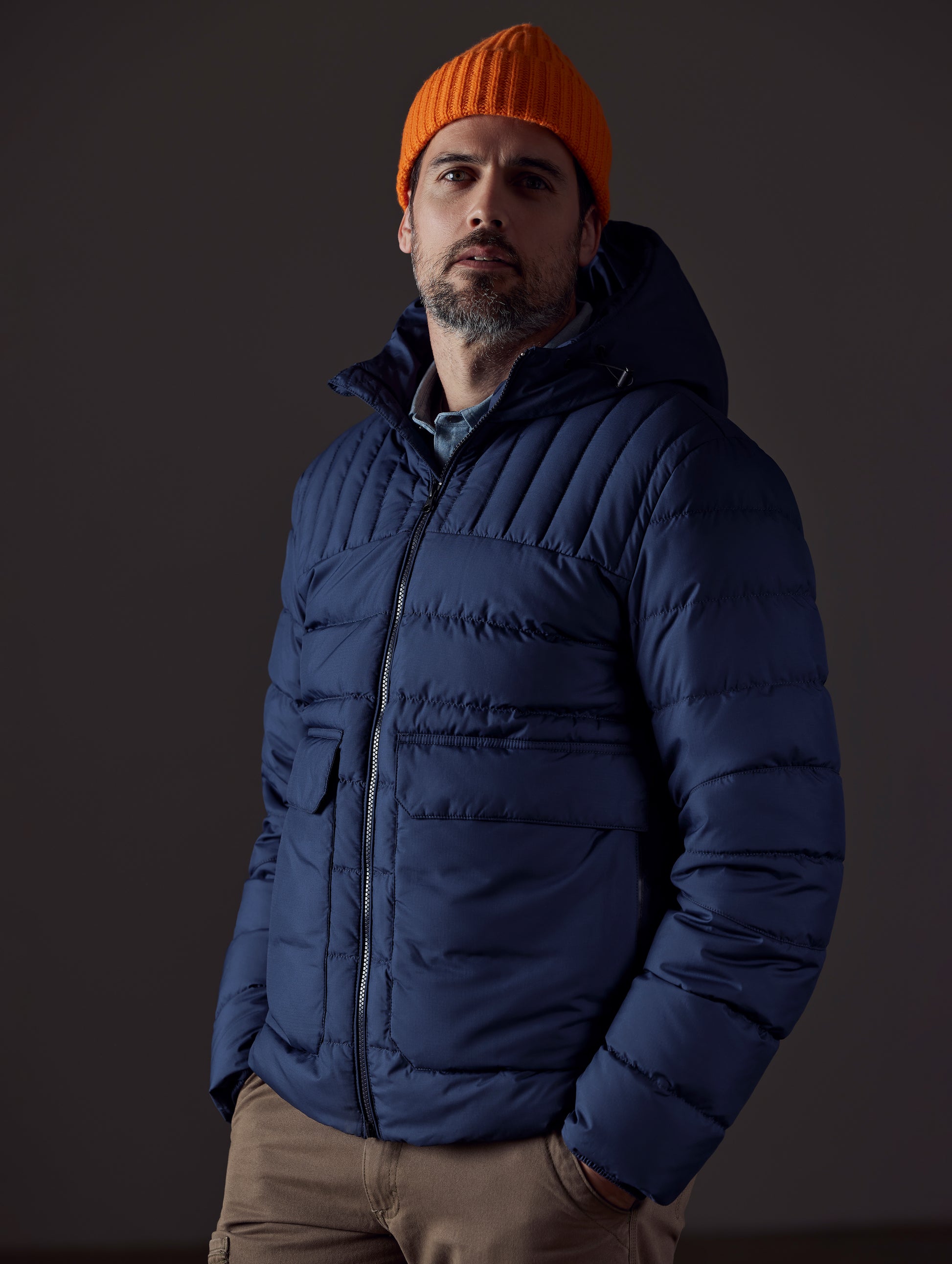 Front 3/4 body view of man with hands in pant pockets wearing Hudson Down Jacket in Total Eclipse dark blue from AETHER Apparel.